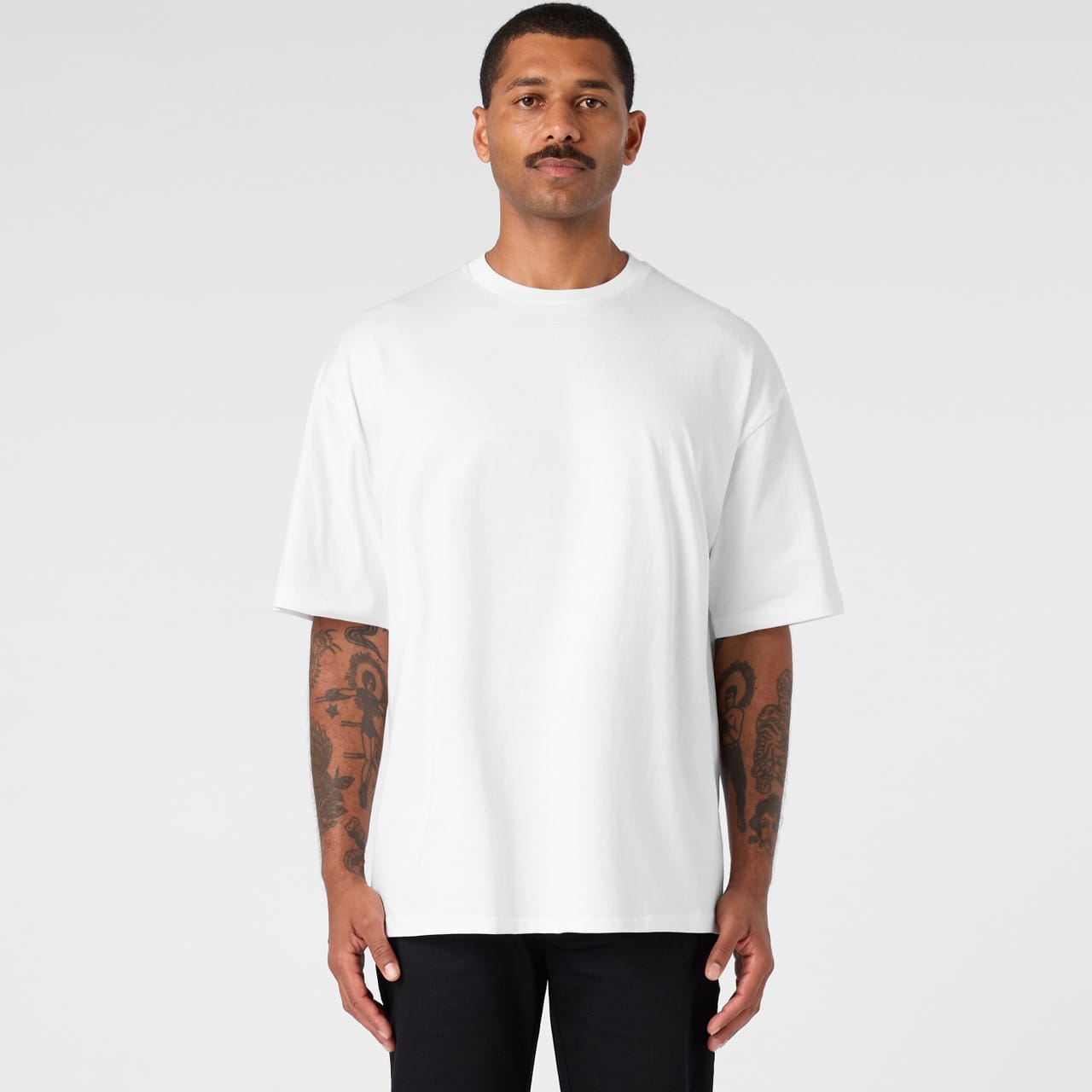 An oversized tee in white worn by a man with tattoos, featuring a simple design and a logo. Block Oversized Tee - Image 1
