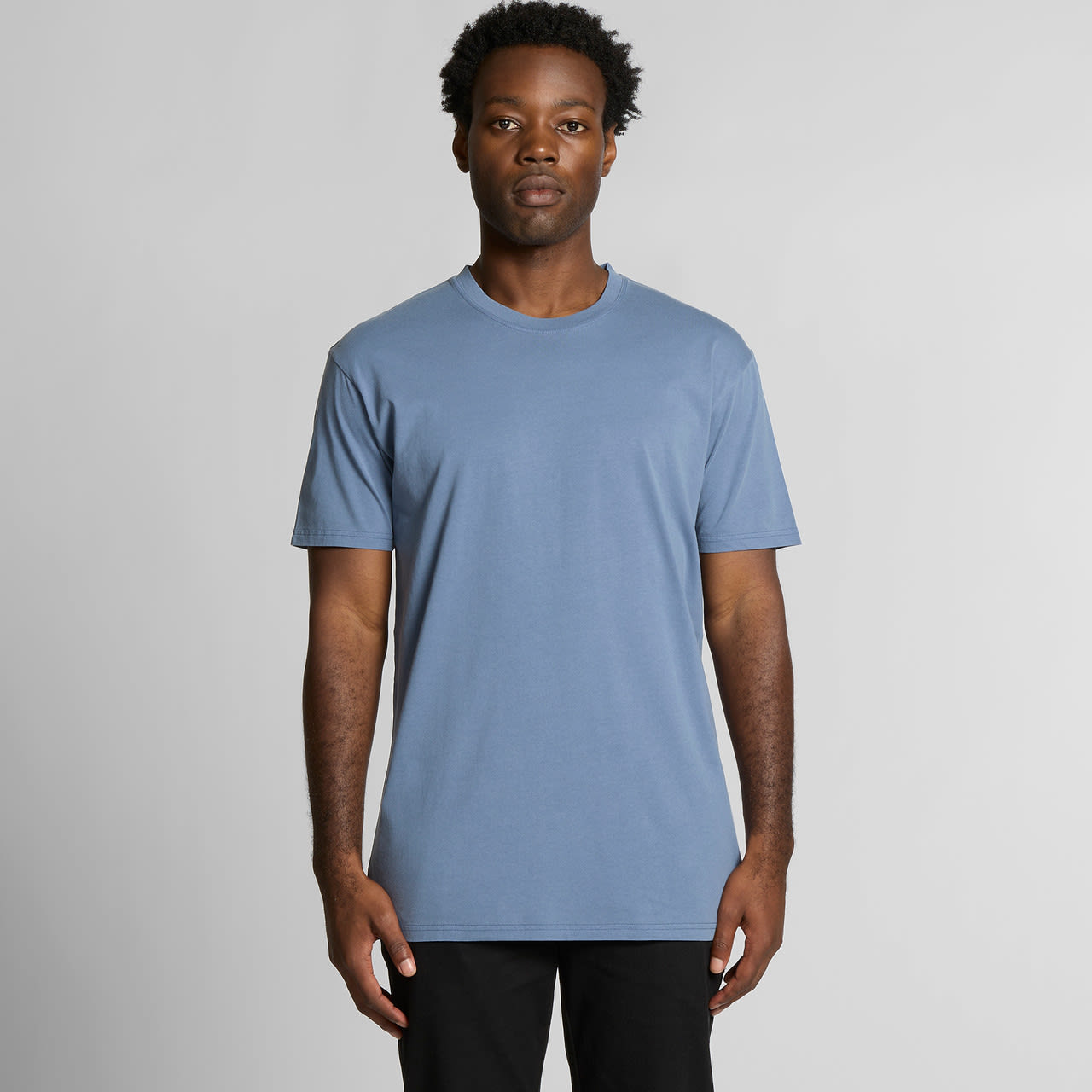 A blue t-shirt featuring a simple design, short sleeves, and a round neck. The model stands against a plain background. Staple Faded Tee - Image 1