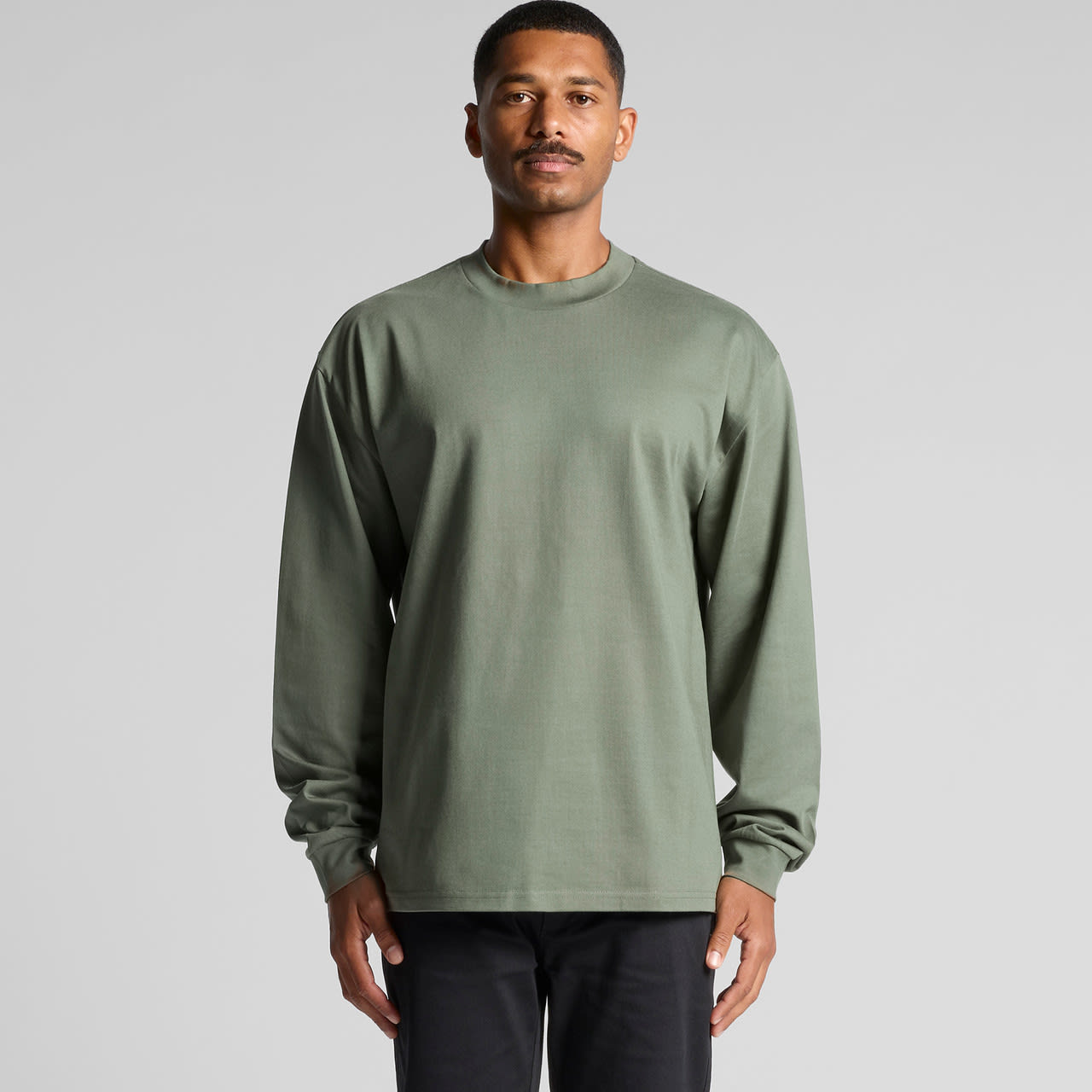 A long-sleeved green T-shirt displayed on a model against a plain background, featuring a logo on one side. Heavy L/S Tee - Image 1