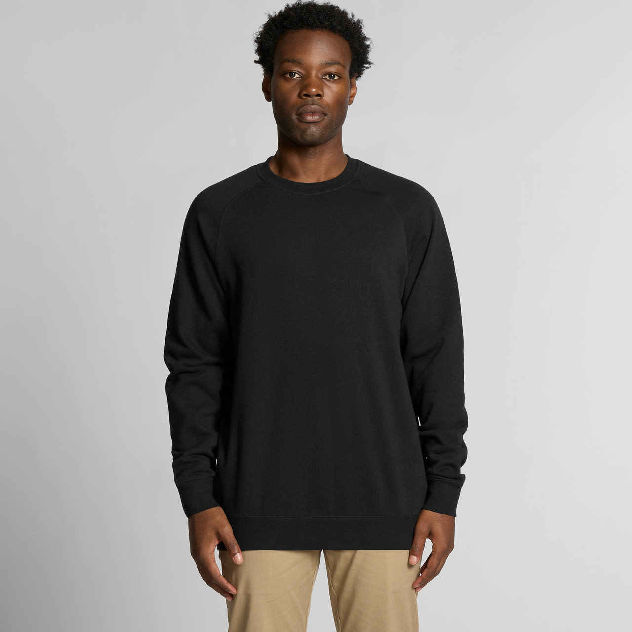 A black jumper is worn by a model with short, curly hair against a neutral background. The garment has a simple design and a logo. Supply Crew - Image 1