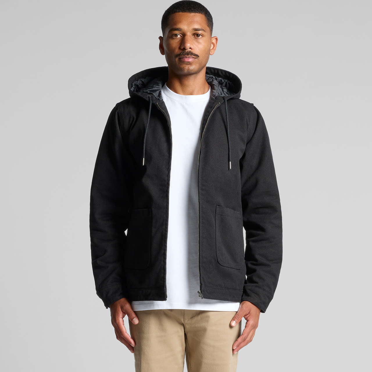 A man wearing a black canvas heavy hooded jacket with zip and front pockets. The jacket has a hood and a grey lining. Canvas Heavy Hooded Jacket - Image 1