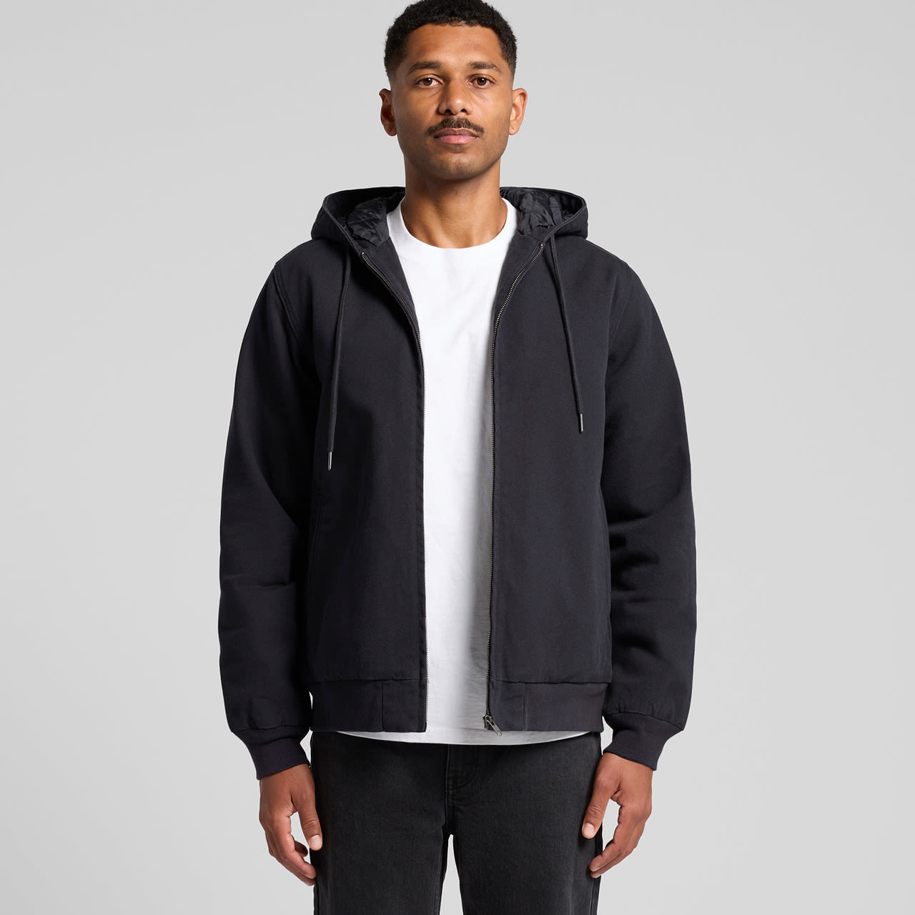 A black canvas bomber hood jacket with a zip front and drawstring hood, worn over a white t-shirt. Canvas Bomber Hood Jacket - Image 1