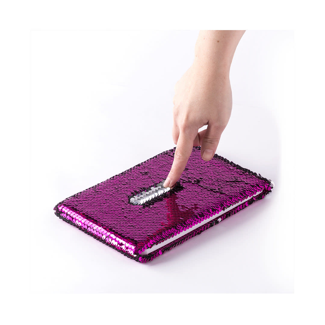 A pink and black sequin notepad with a sparkling surface, being touched by a hand. It features a logo. Velmont Notepad - Image 1