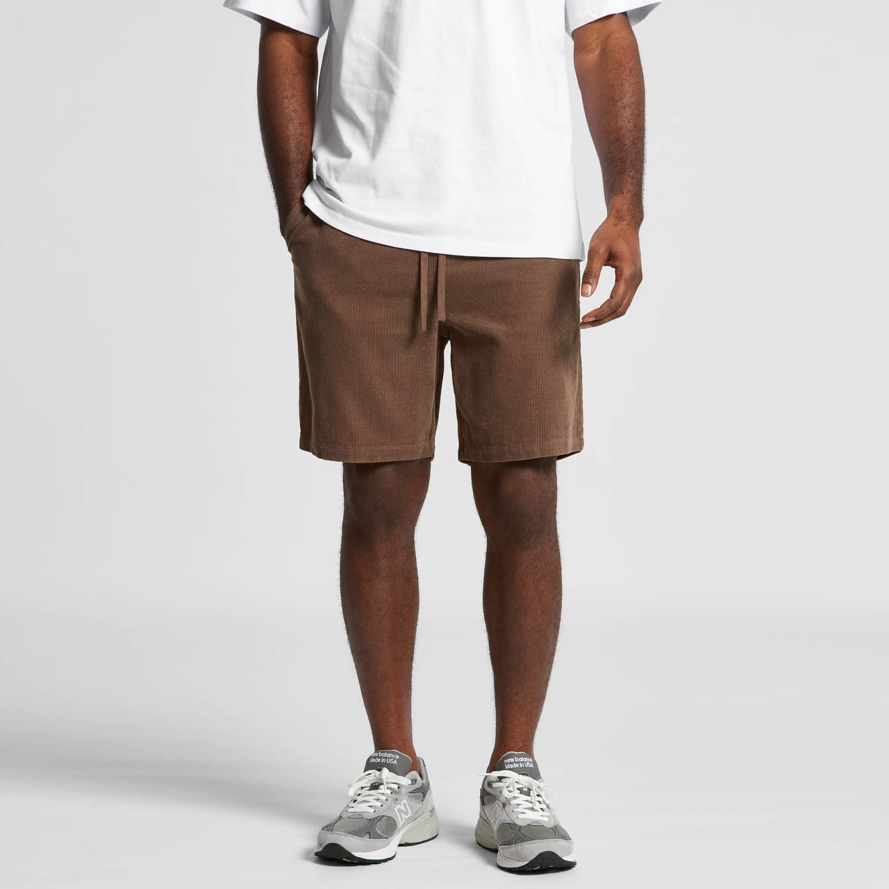 Brown dress shorts with side pockets and a drawstring waist, worn with a plain white shirt and grey sneakers. Cord Shorts 18" - Image 1