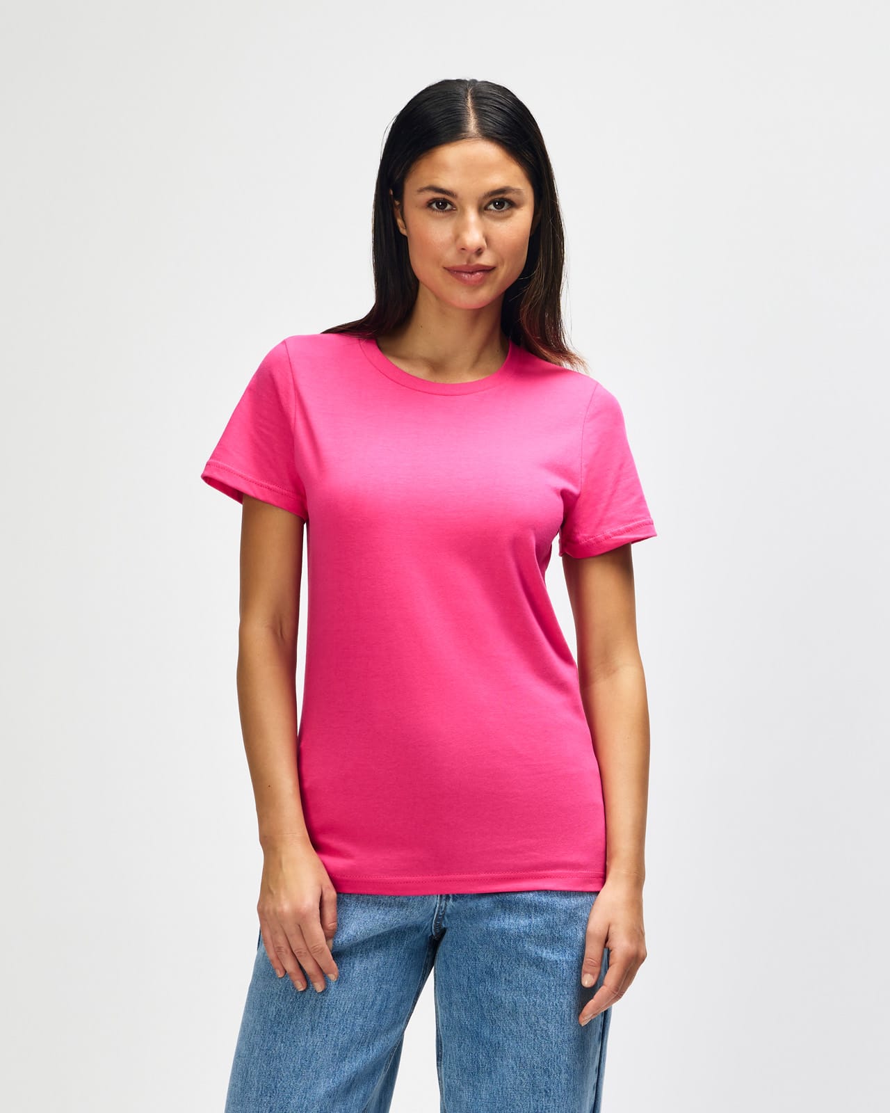 A pink Gildan Softstyle ladies midweight T-shirt displayed on a model, featuring a simple design and a logo. Gildan Softstyle Ladies Midweight T-Shirt - Image 1