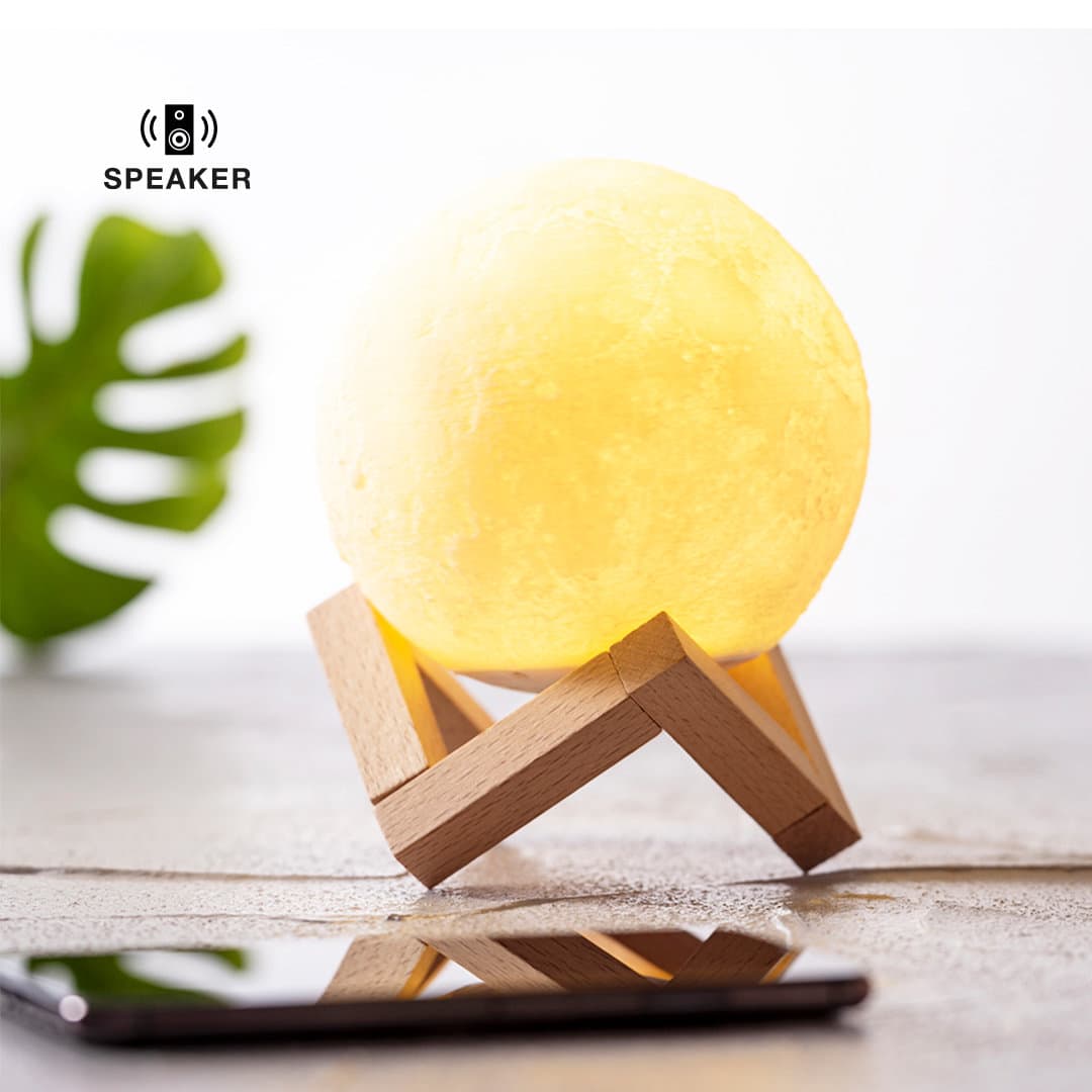 A round yellow moon-shaped speaker sits on a wooden stand beside a smartphone on a surface. Yois Speaker - Image 1