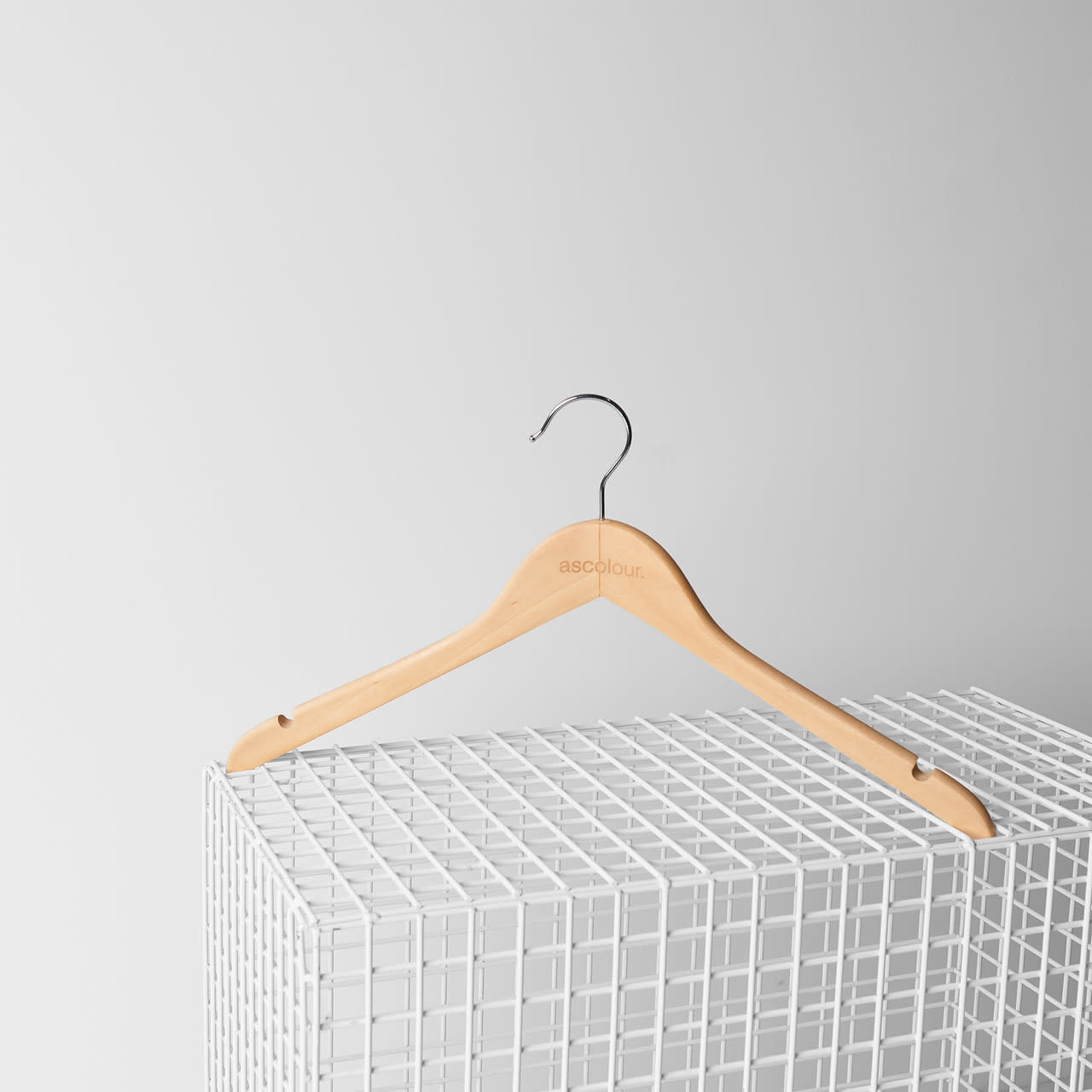 A wooden hanger with a silver hook, featuring a logo, resting on a white wire grid. AS Logo Hanger | 6840 - Image 1