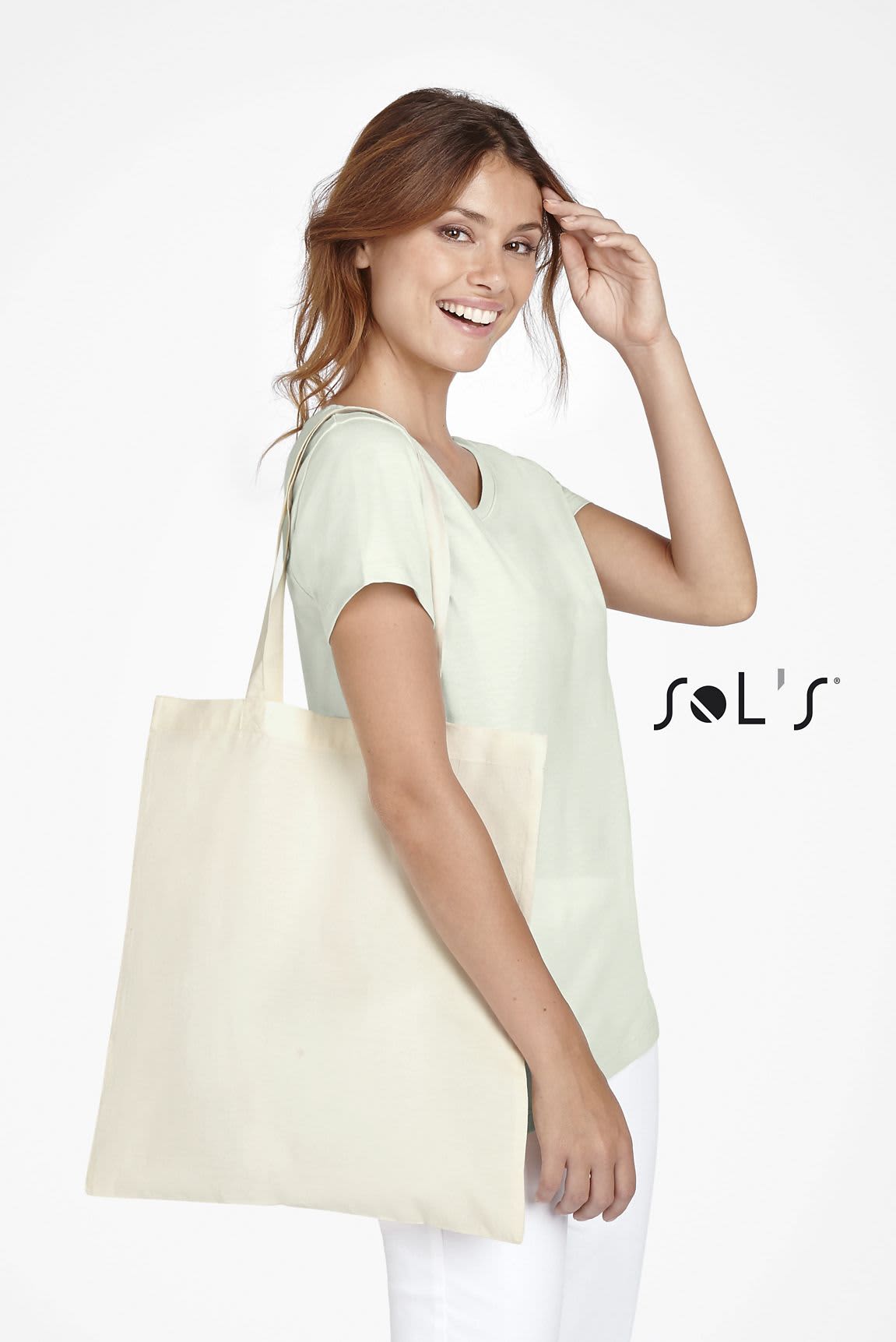 A person holds a natural beige tote bag, wearing a light green top and smiling, with a logo visible on the bag. ORGANIC ZEN SHOPPING BAG - Image 1
