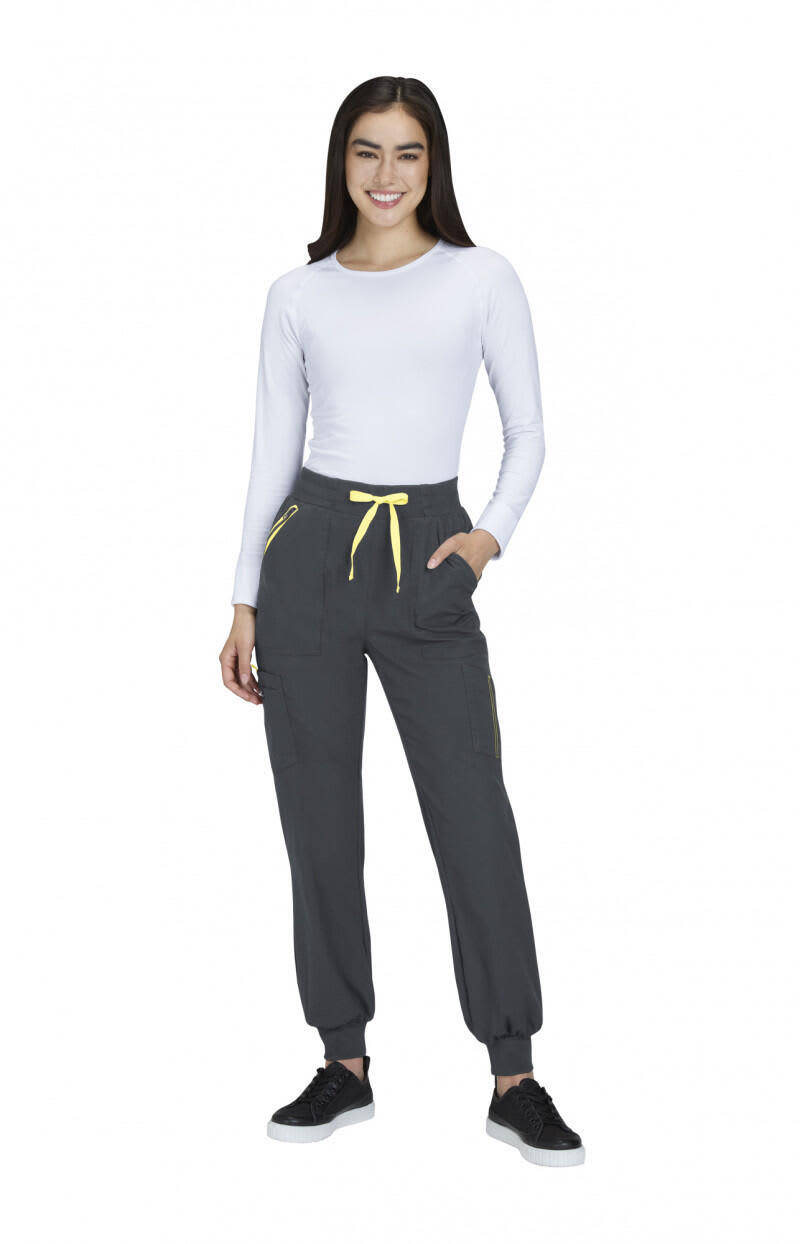 A woman wearing grey joggers with yellow drawstrings and pockets, paired with a white long-sleeve top and black shoes. Hettie Jogger - Image 1