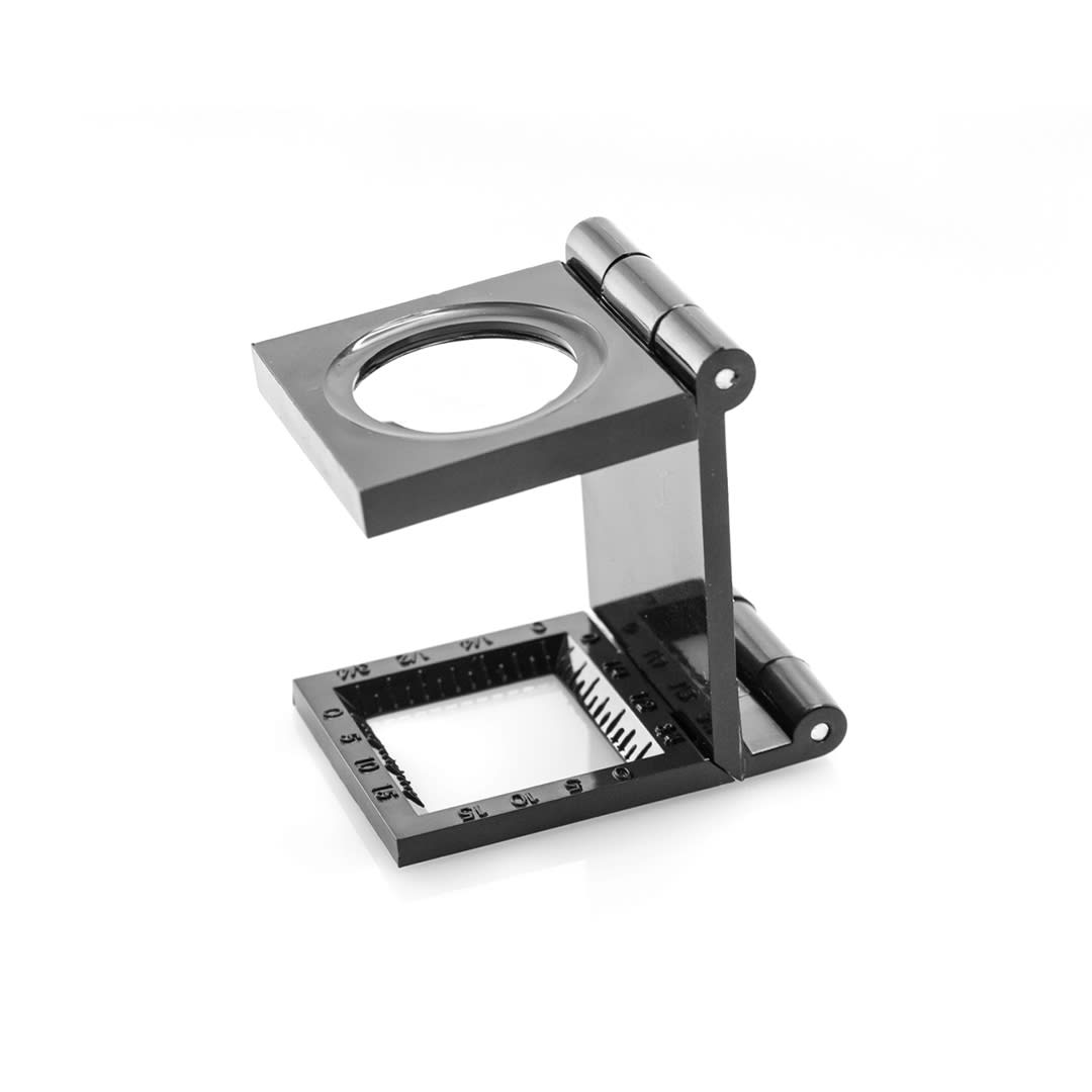 A black magnifier with a hinged design, featuring a circular lens and a square base marked with measurements. Mauran 7X Magnifier - Image 1