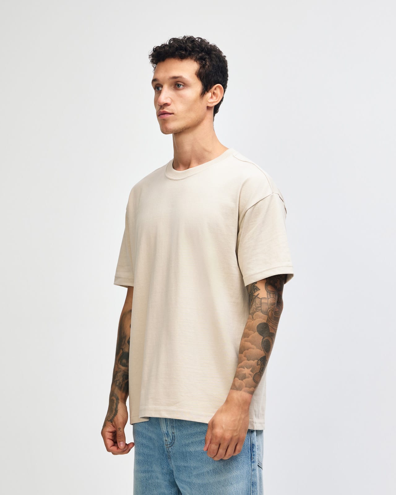 A beige super heavyweight T-shirt displayed on a model, featuring a relaxed fit and short sleeves. American Apparel Super Heavyweight T-Shirt - Image 1