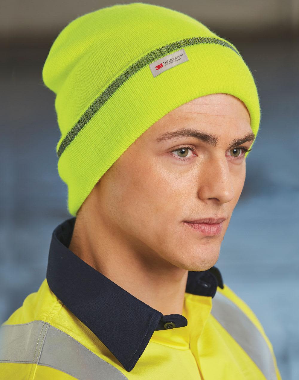 A bright neon yellow cuff beanie with a grey stripe, fitted snugly on a model's head. It features a brand logo tag. 3M Insulated Beanie with Reflective stripe - Image 1