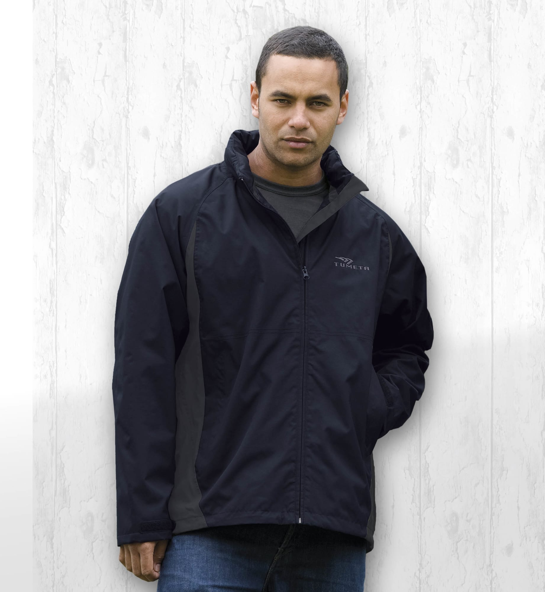 A man wearing a black jacket with a logo, set against a light wood background. Crosswinds Jacket - Image 1