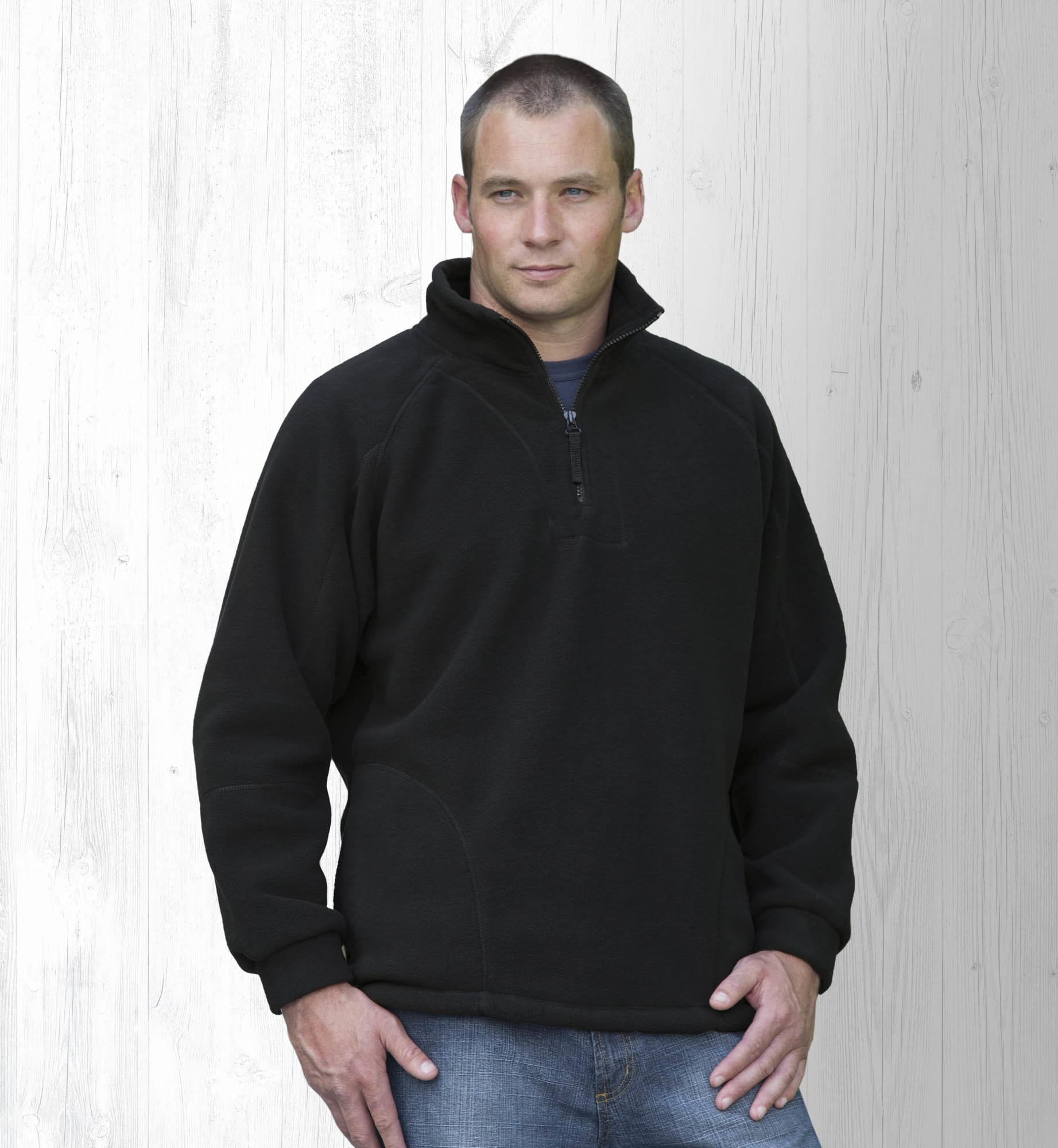 A man wearing a black polar fleece pullover with a half zip, standing against a light wooden background. Detailed Polar Fleece Pullover - Image 1