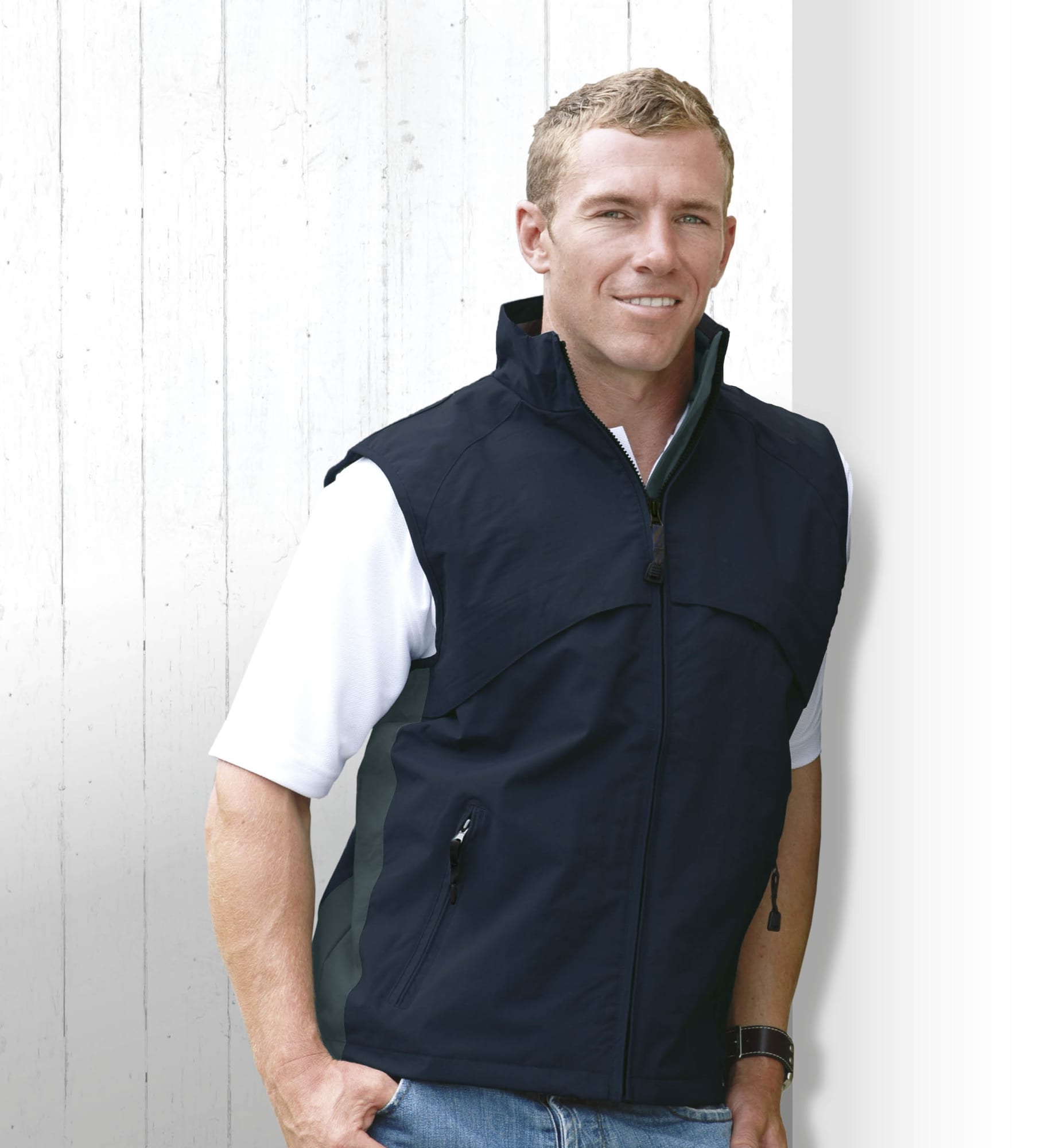 A man wearing a black vest, standing against a white wooden background. The vest features a zip and side pockets. Gravity Vest - Image 1