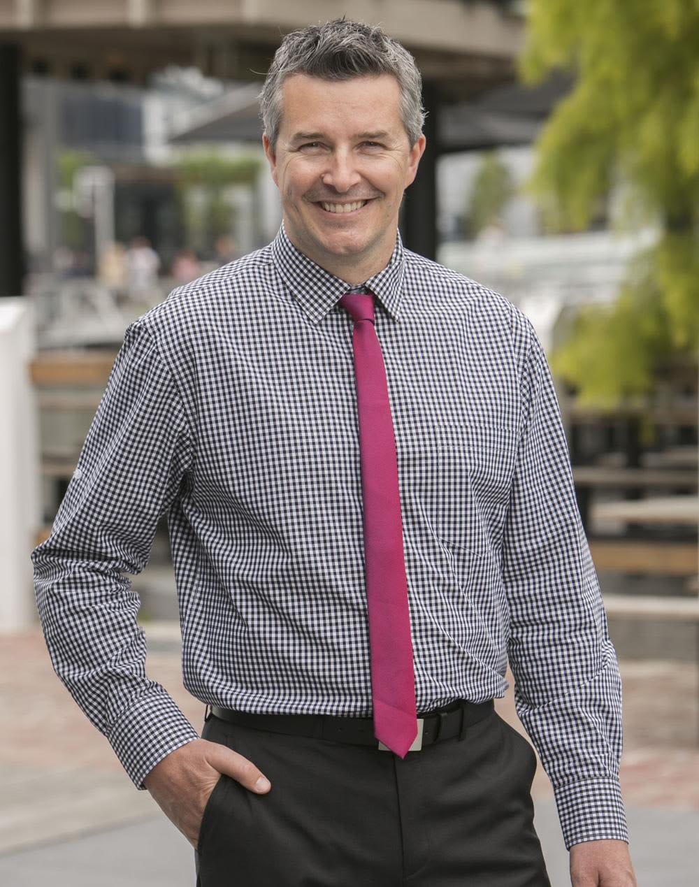 A man in a blue and white gingham check long-sleeve button-up shirt, wearing a pink tie and black trousers. Men's Gingham Check Roll-up L/S Shirt - Image 1