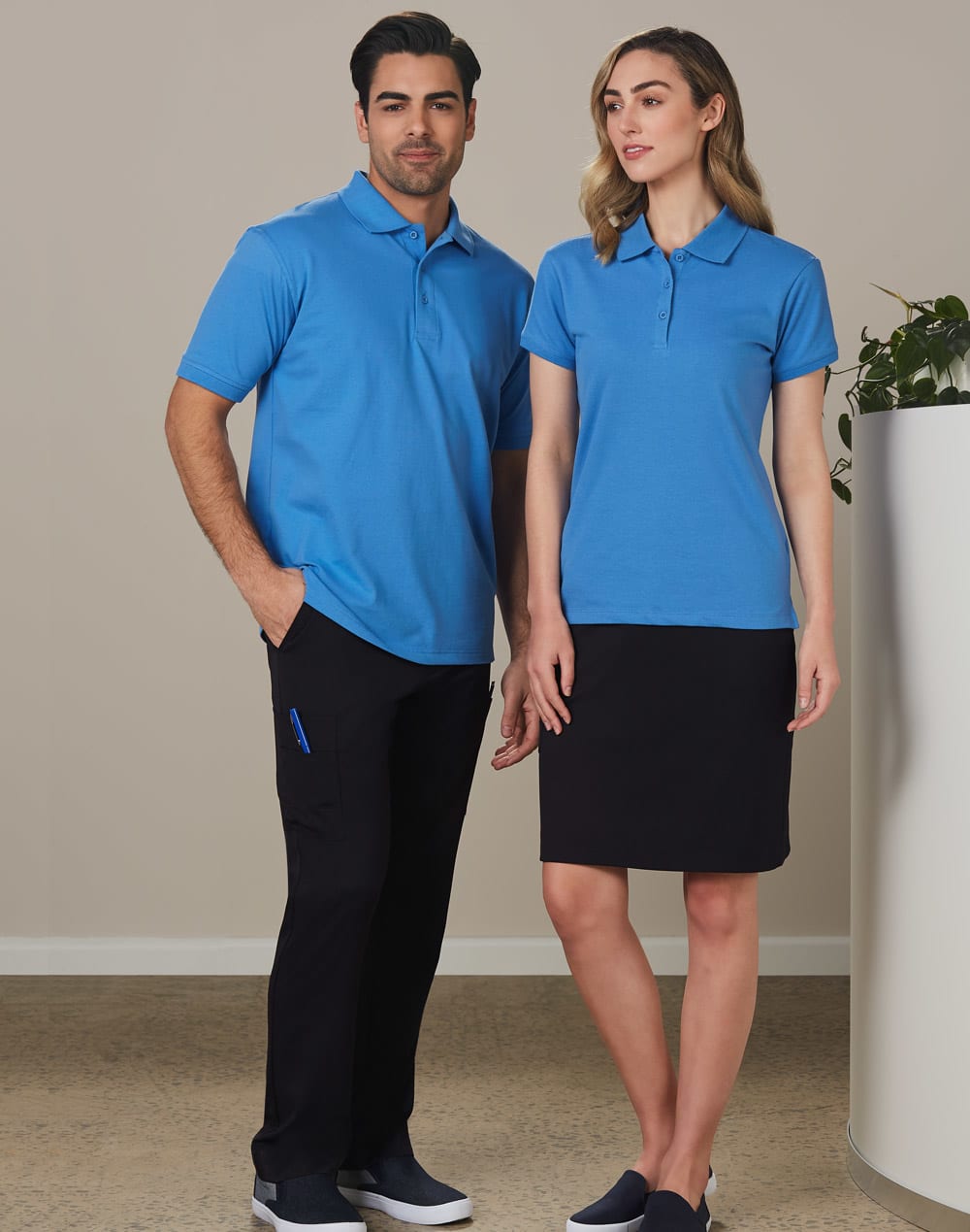 A man and woman standing together, wearing matching blue polo shirts. The man pairs his top with black cargo pants, while the woman wears a black skirt. Men's Utility Cargo Pants - Image 1