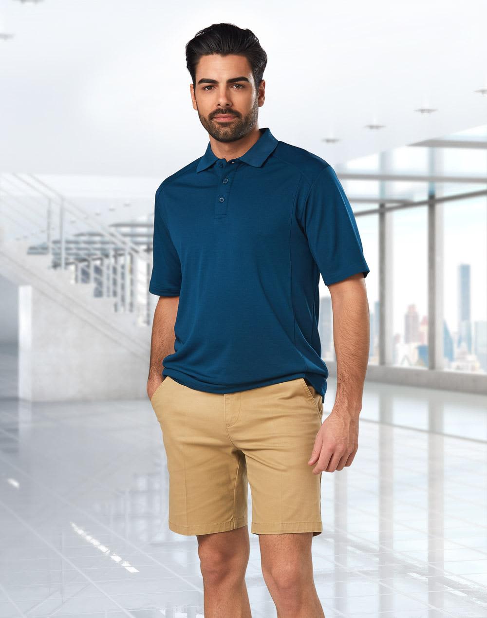 Men's stretch cotton chino shorts in khaki, paired with a navy polo shirt. The model stands in a modern indoor setting. Men's Stretch Cotton Chino Shorts - Image 1