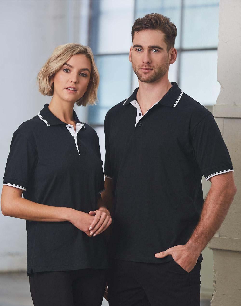 A unisex black polo shirt featuring white detailing, modelled by a man and woman in an indoor setting. unisex cotton jersey polo - Image 1