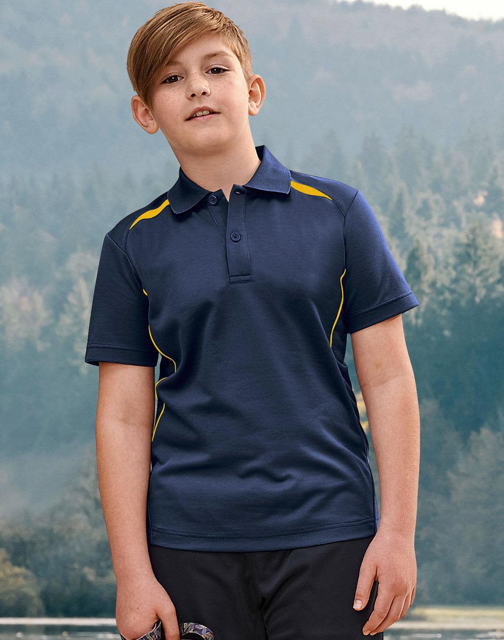 A boy stands outdoors wearing a navy polo shirt with yellow accents and a logo. The background features trees and hills. Kids' Sustainable Poly/Cotton Contrast S/S Polo - Image 1