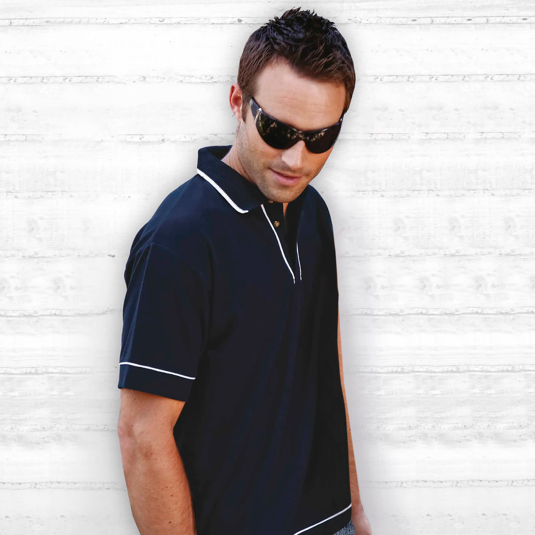 A black polo shirt with white trim displayed on a model wearing sunglasses. The shirt has a collar and a logo. Retro Waffle Polo - Mens - Image 1