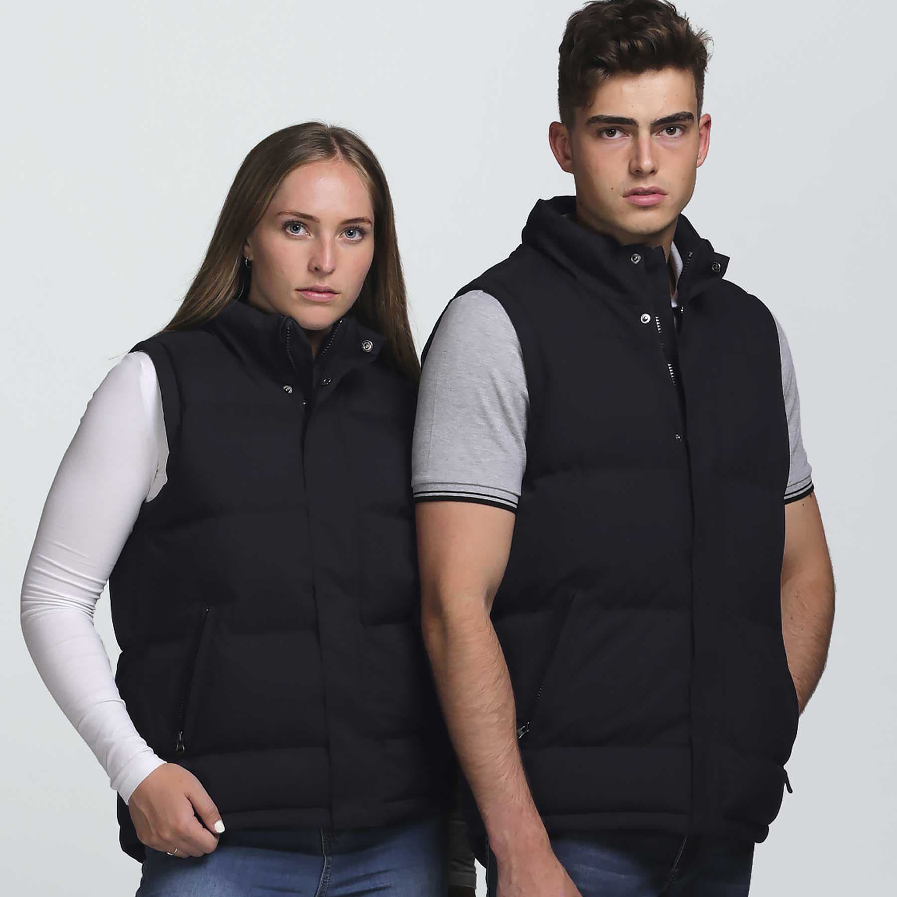 A black puffa vest is displayed on two individuals, featuring a zip-up design and pockets. smpli Junction Puffa Vest - Image 1