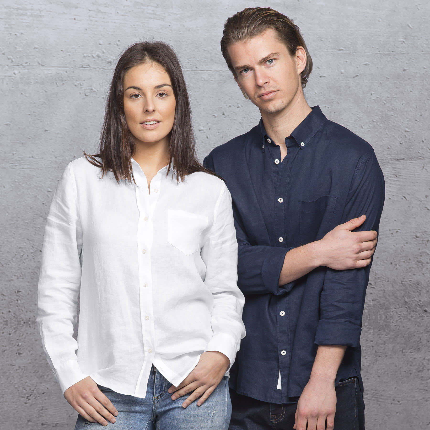 A white linen button-up shirt worn by a woman and a navy button-up shirt worn by a man, both against a textured background. smpli Womens Linen Shirt - Image 1