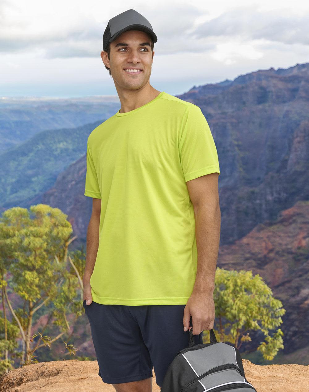 A man wearing a bright yellow short-sleeve performance T-shirt stands against a mountainous backdrop, holding a bag. Men's Ultra Light Weight Performance S/S Tee - Image 1