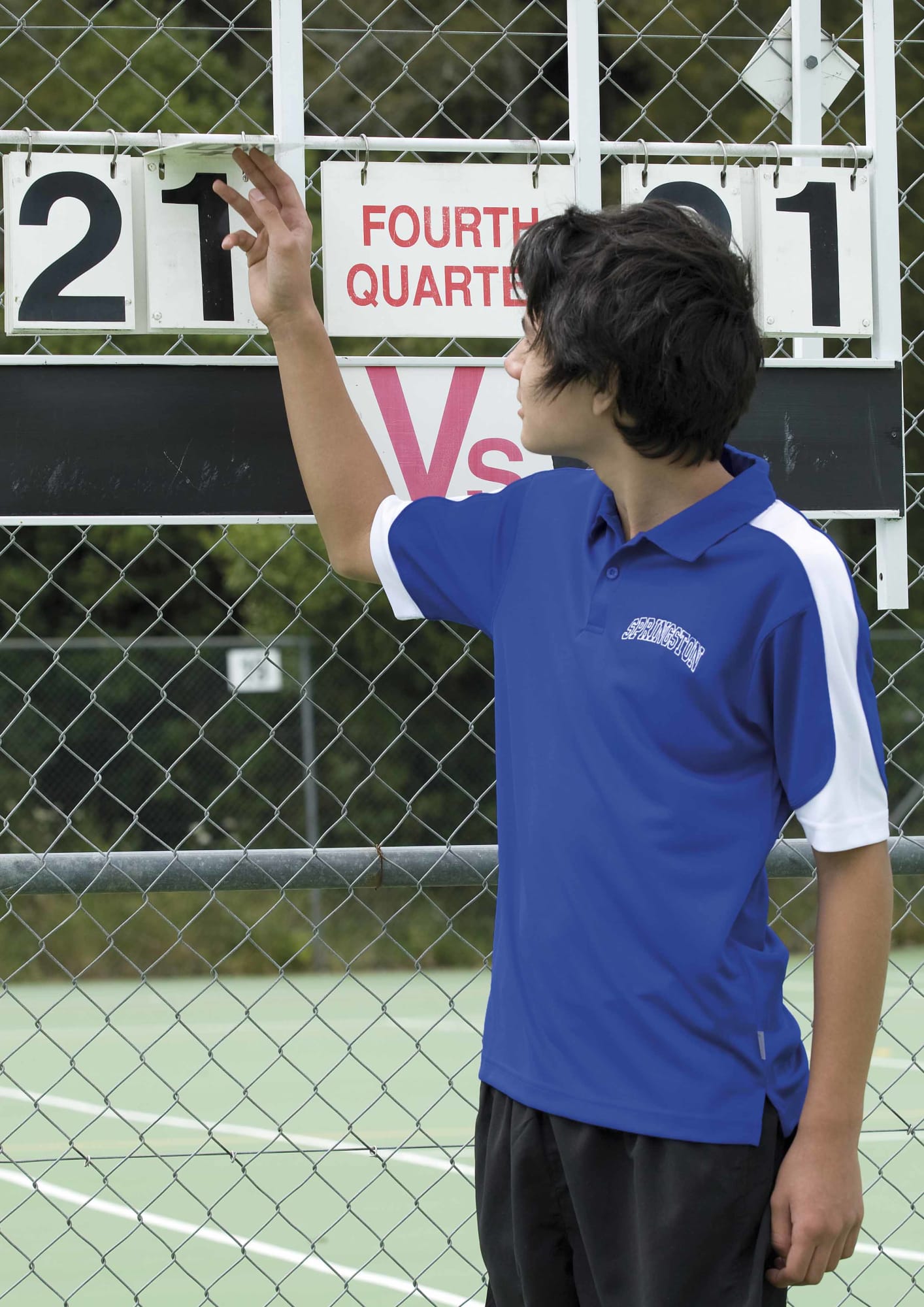 A young person adjusts a scoreboard while wearing a blue and white polo shirt with a logo. Youth Dri Gear Challenger Polo - Image 1