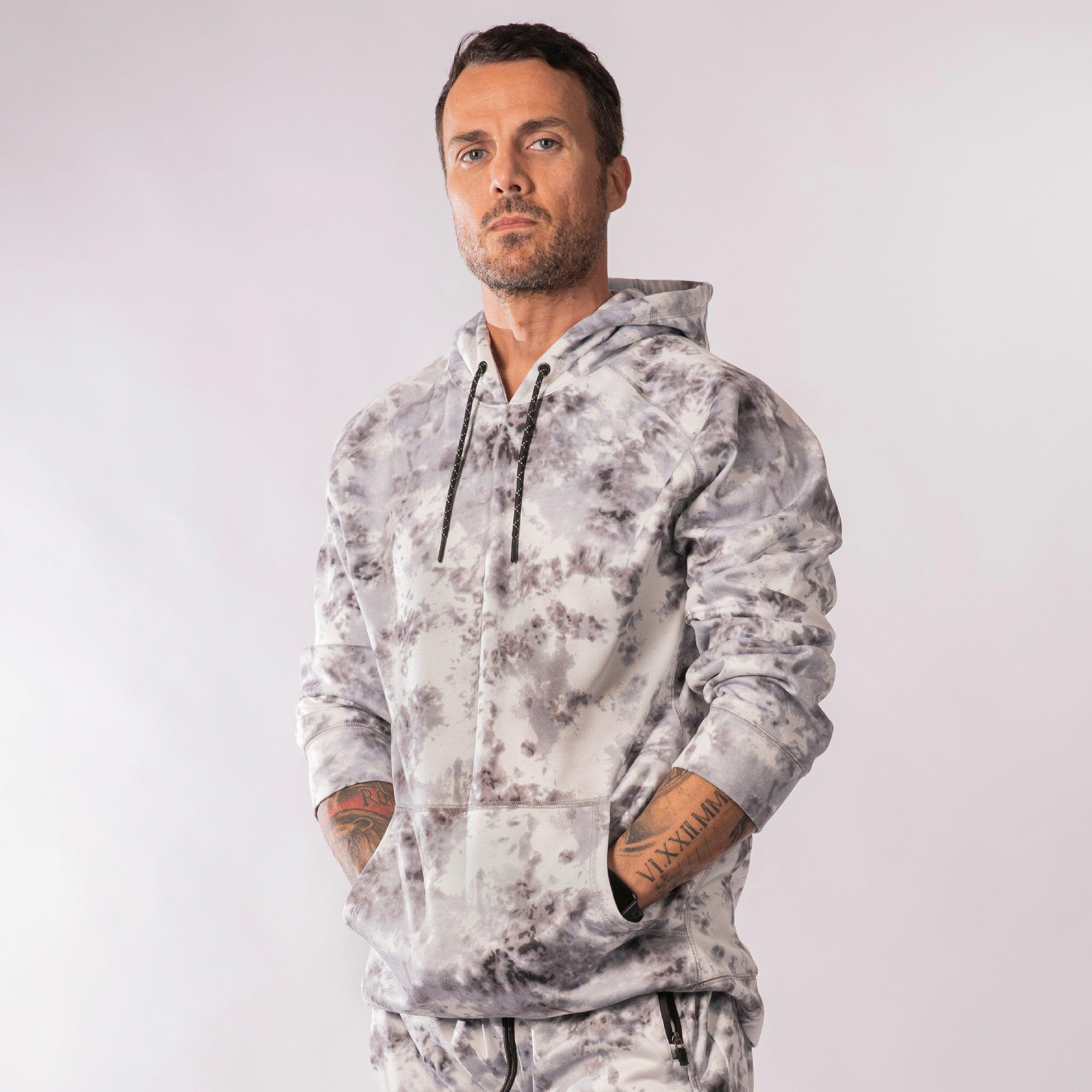 A tie-dye patterned pullover hoodie in grey tones, featuring a logo and a drawstring hood. Performance Raglan Pullover Hoodie - Image 1