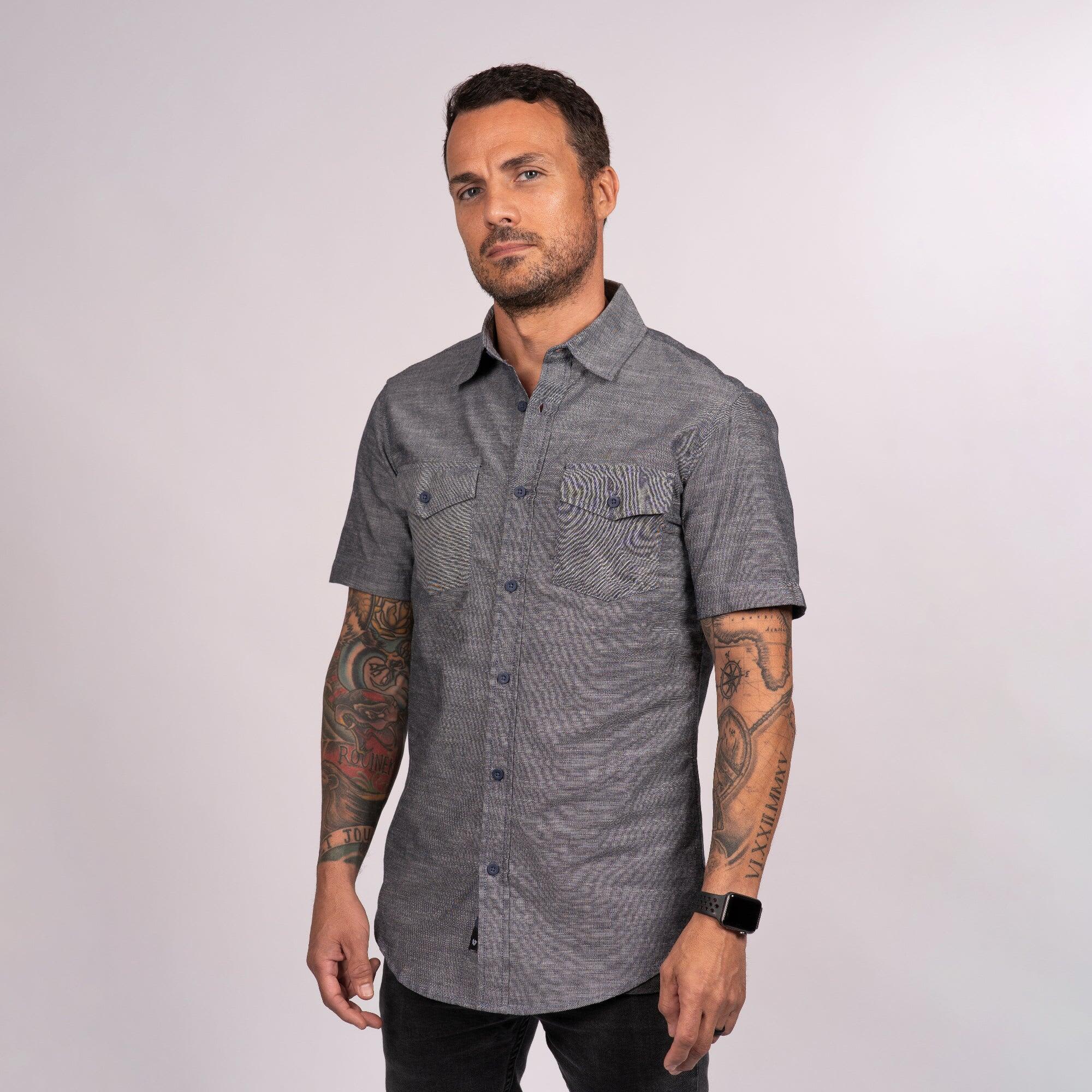 A man wearing a short sleeve chambray shirt in grey, featuring a pocket and a logo. Short Sleeve Chambray Shirt - Image 1