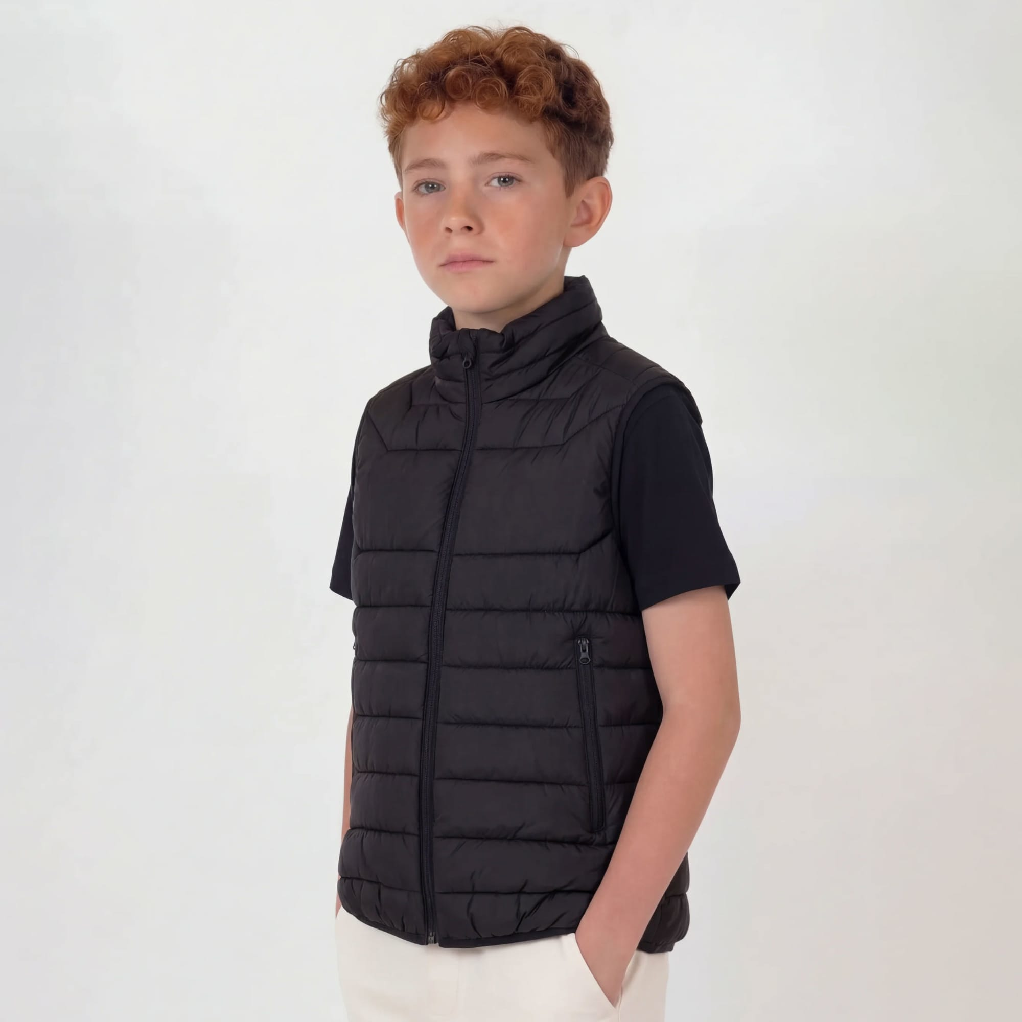 A youth puffer vest in black, featuring a zip-up front and high collar, worn by a young boy against a neutral background. Youth Proper Puffer Vest - Image 1
