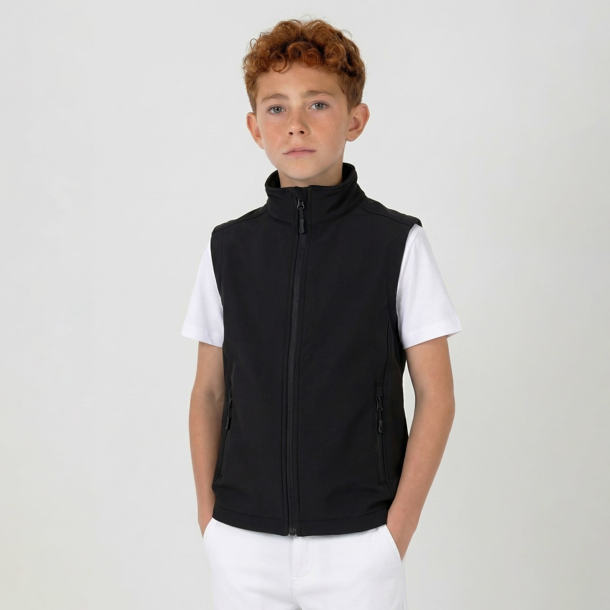 A youth softshell vest in black, featuring a zip front and high collar, worn over a white shirt. Youth Prime Softshell Vest - Image 1