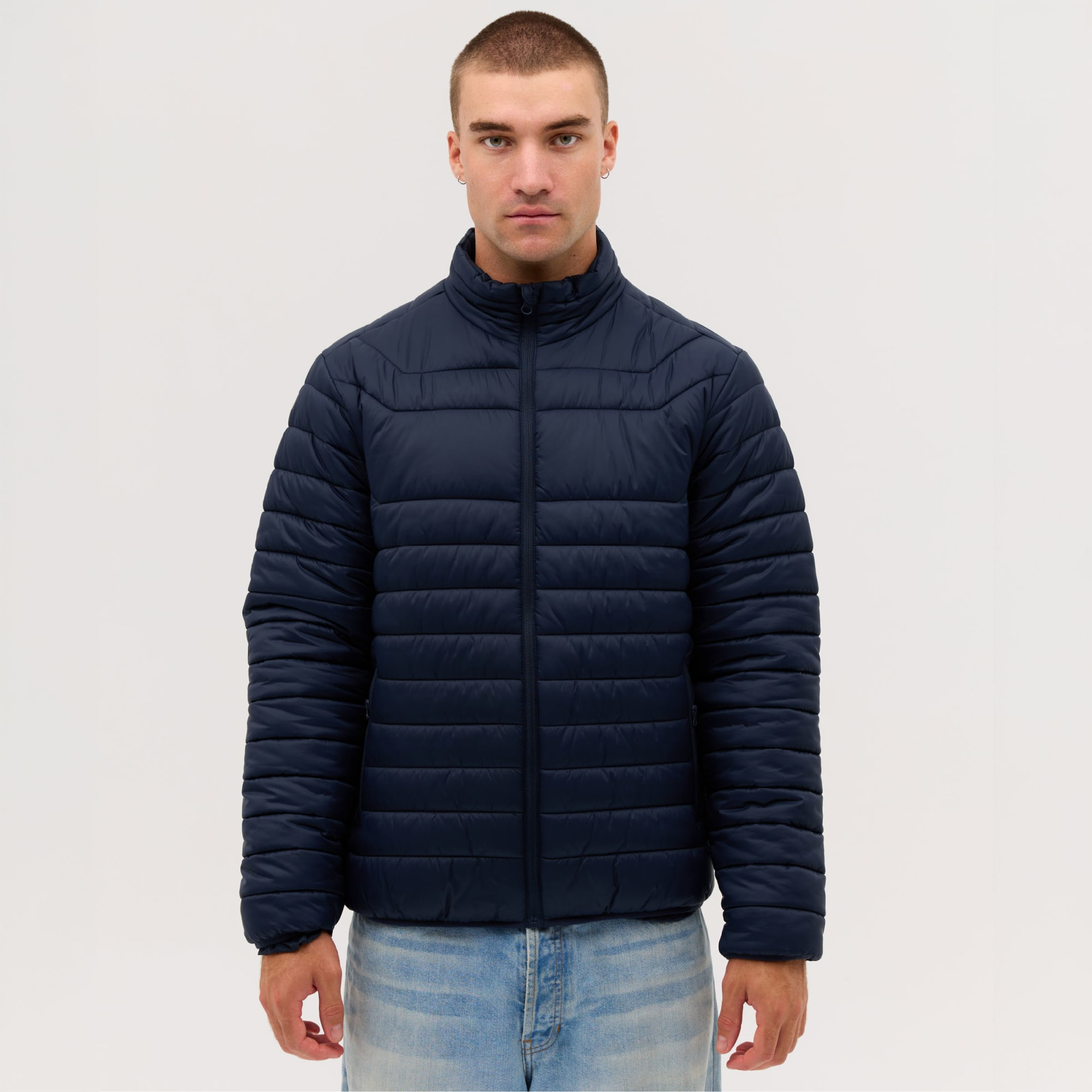 A navy puffer jacket with a high collar and zippered front, displayed on a male model against a plain background. Proper Puffer Jacket - Image 1