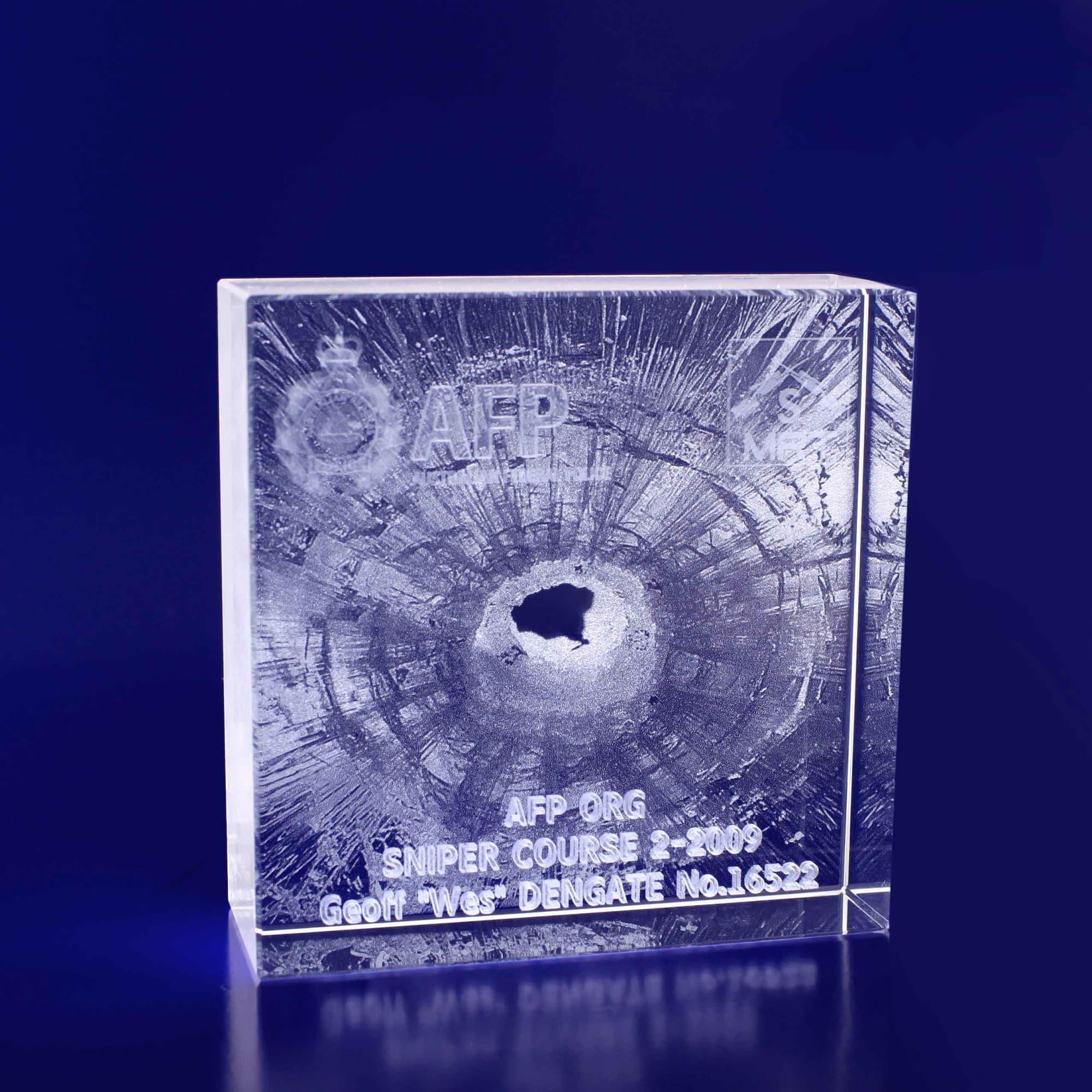 A clear 3D crystal square, 100x100x35mm, featuring a round hole and a logo. The surface has textured detail. 3D Crystal Square 100x100x35mm - Image 1