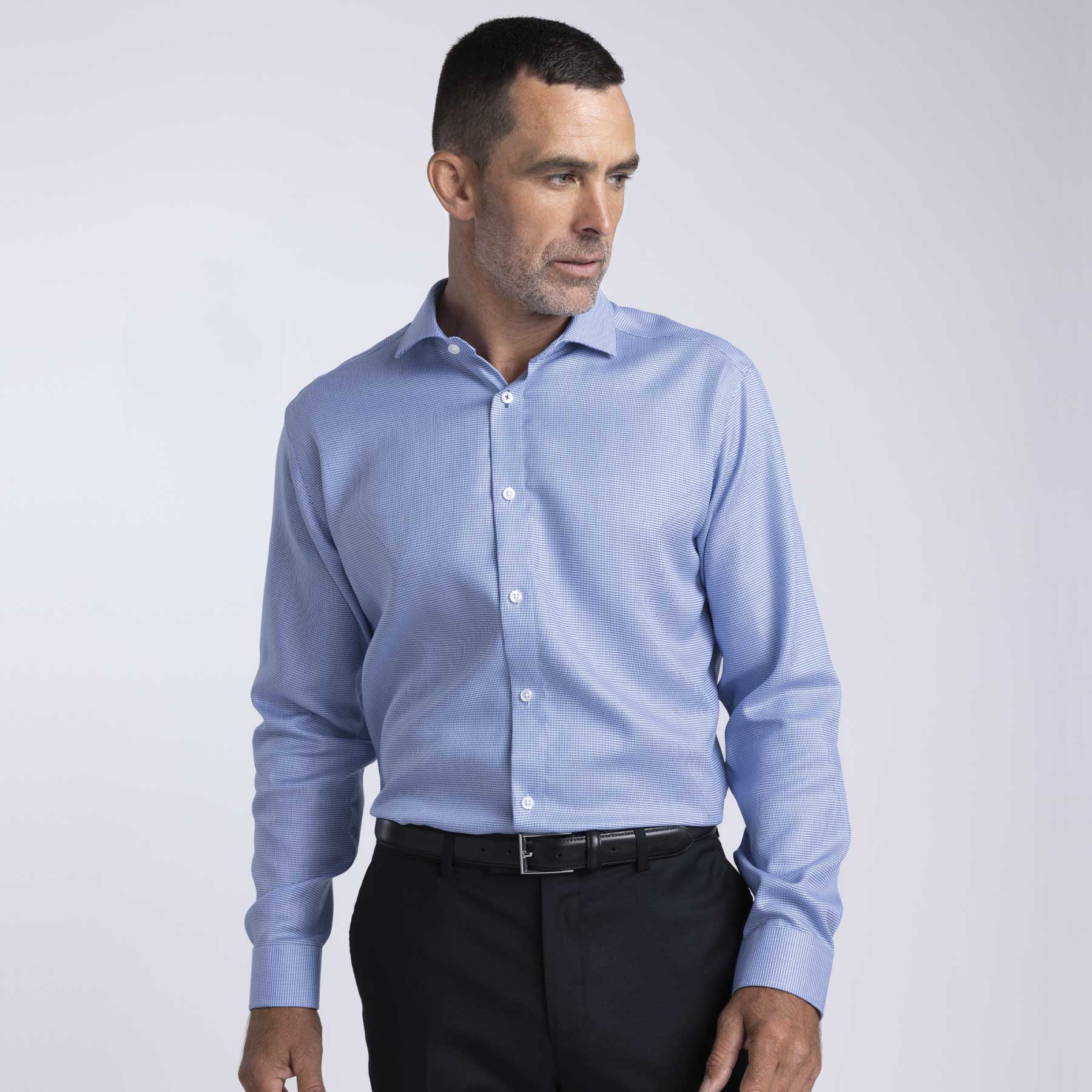 A men's button-up shirt in light blue fabric, featuring a collar and buttons, worn with black trousers. Barkers Corporate Quadrant Shirt – Mens - Image 1