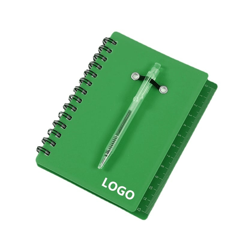 A green mini notebook with a spiral binding and a ballpoint pen attached, featuring a ruler along the edge. Mini Notebook with Ballpoint Pen - Image 1