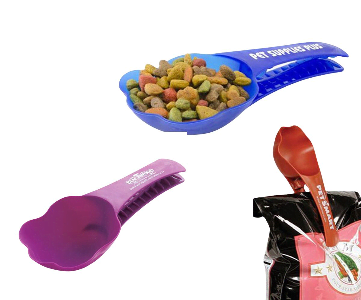 A blue and a purple pet food clip scooper with kibble, alongside a red scooper, placed near a pet food bag. Pet Food Clip Scooper - Image 1