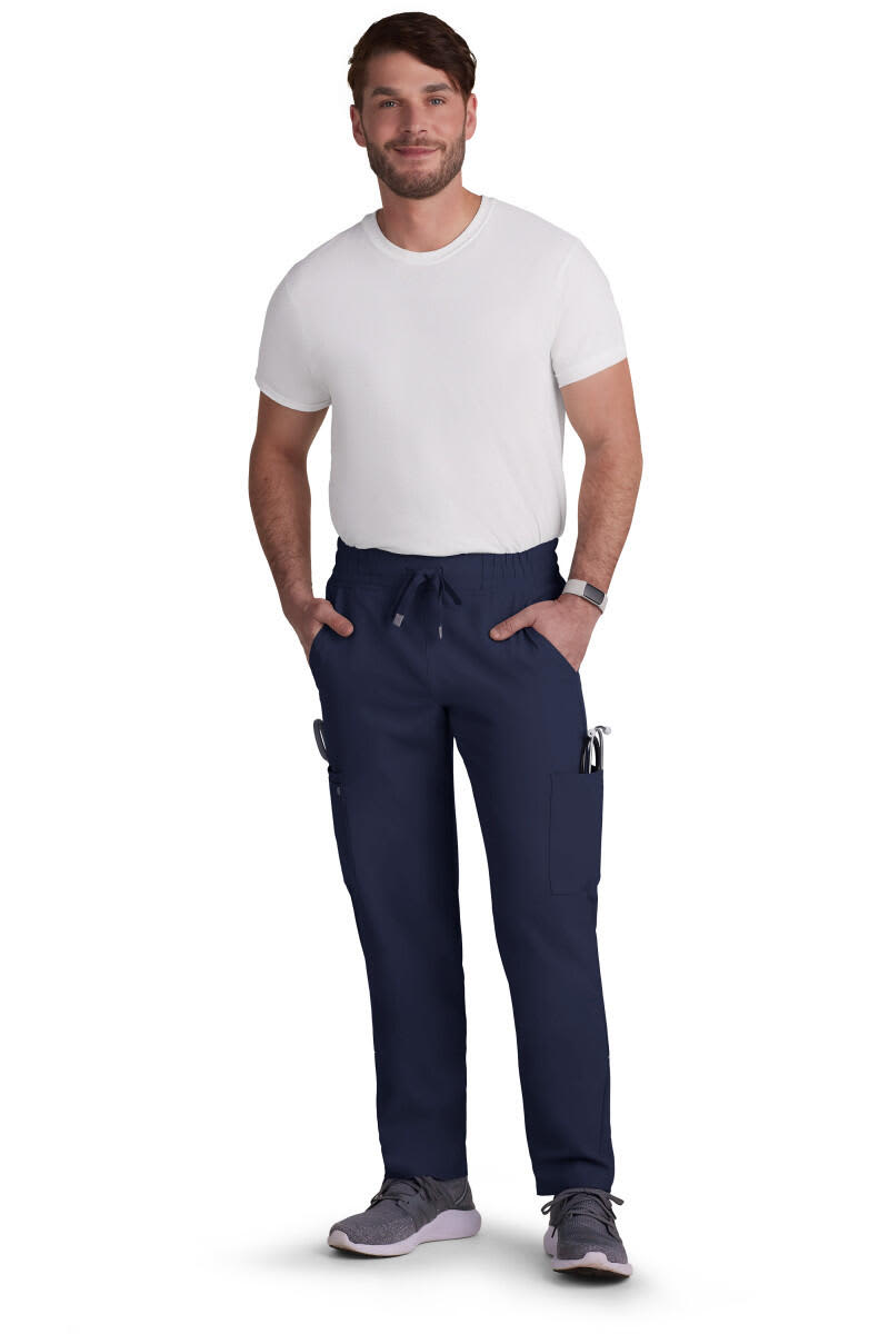 A man in navy neuro cargo pants with pockets, paired with a white T-shirt and grey shoes. The pants have a branding logo. Neuro Cargo Pant - Image 1
