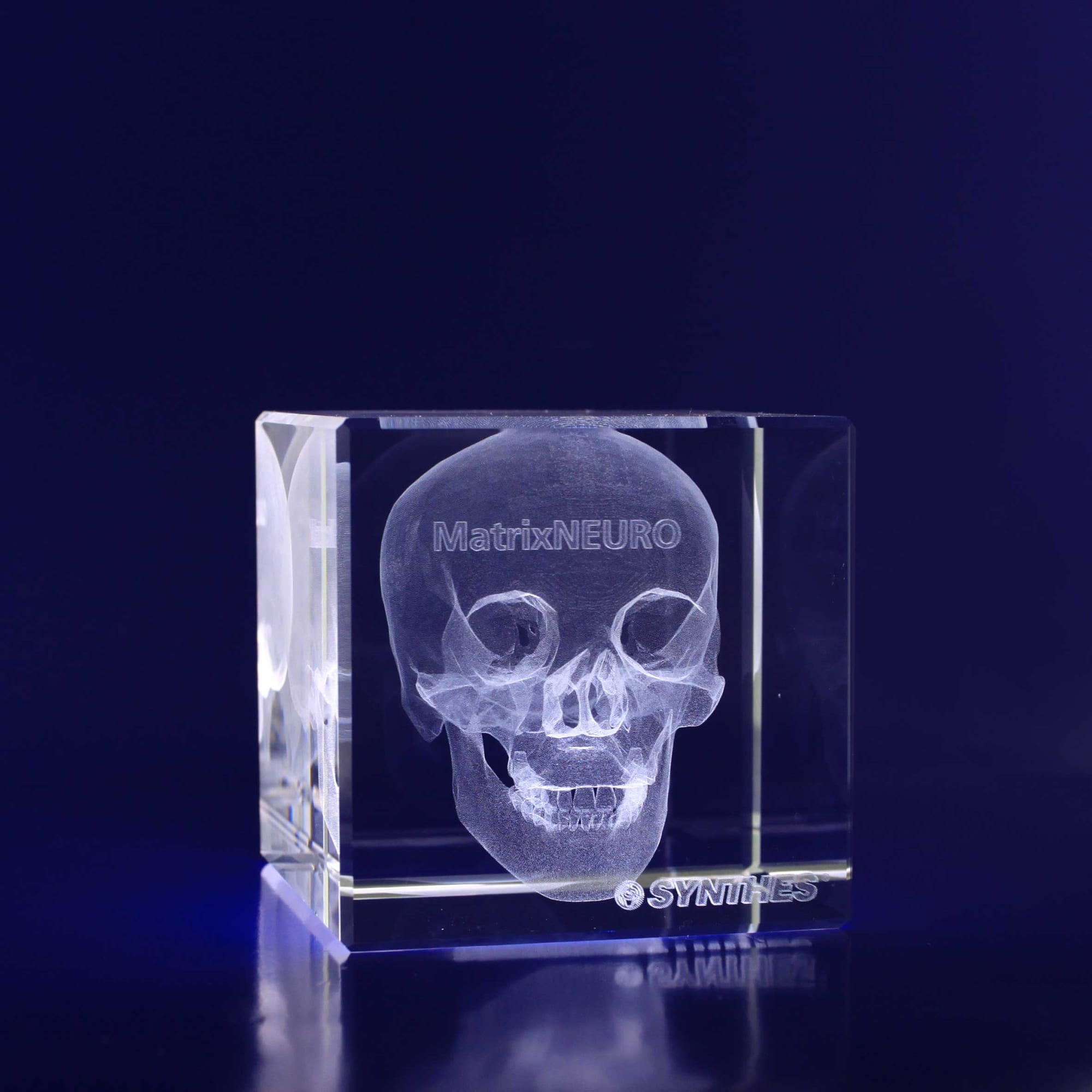 A clear 3D crystal cube featuring an engraved skull design, displayed against a dark background. 3D Crystal Cube (60mm) - Image 1
