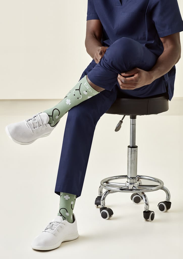 Unisex green socks with a playful design, featuring patterns, worn by a person seated on a stool. Unisex Happy Feet Comfort Socks - Image 1