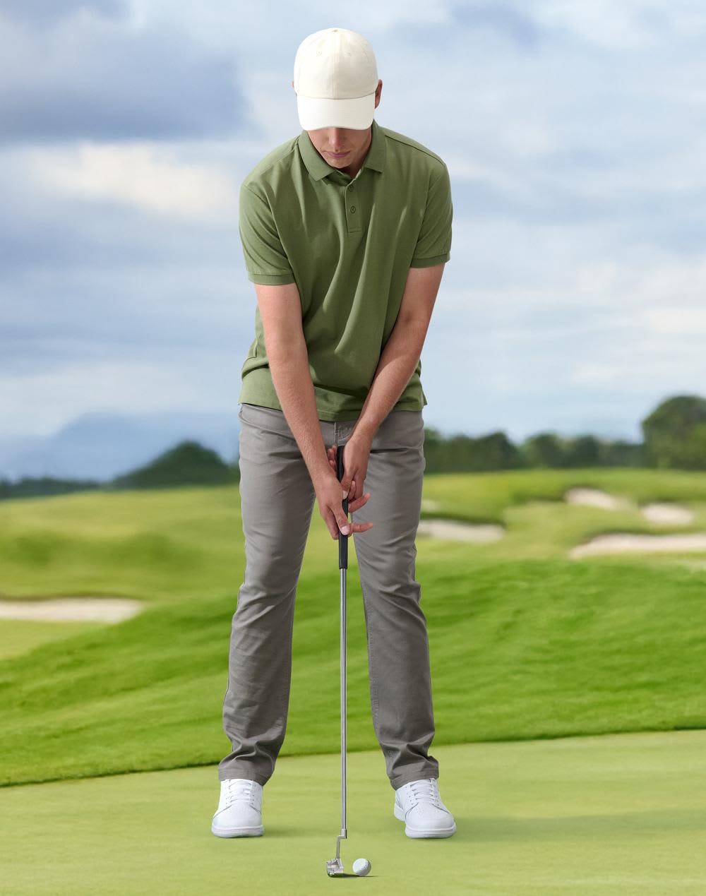 A golfer is putting on a green golf course, wearing a light-coloured cap, green polo shirt, and grey trousers. Cotton Twill Unstructured Cap - Image 1