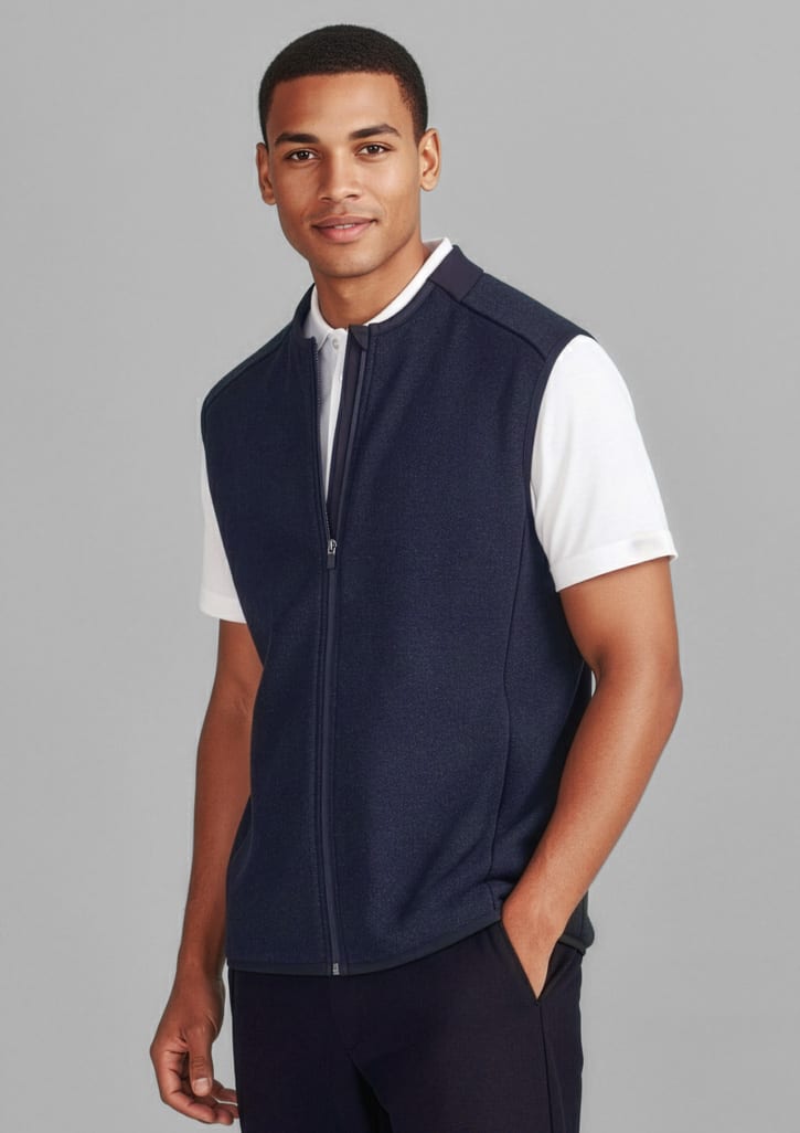 A navy zip-front vest is worn over a white shirt. The model stands against a grey background, featuring a logo on the vest. Mens Nova Zip Front Vest - Image 1