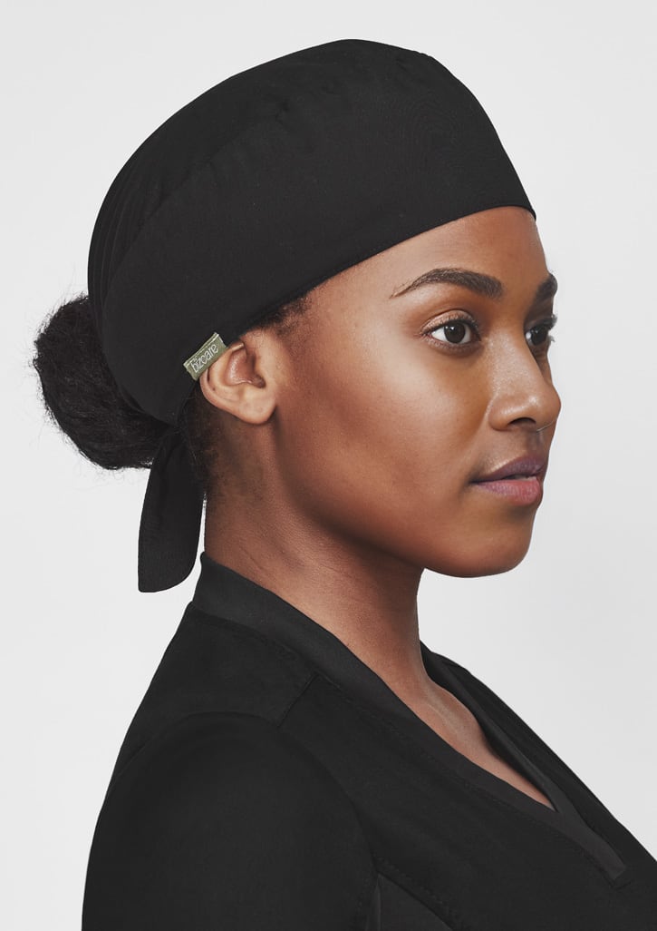 A black unisex reversible scrub cap worn by a person, featuring a logo on the side. Unisex Reversible Scrub Cap - Image 1