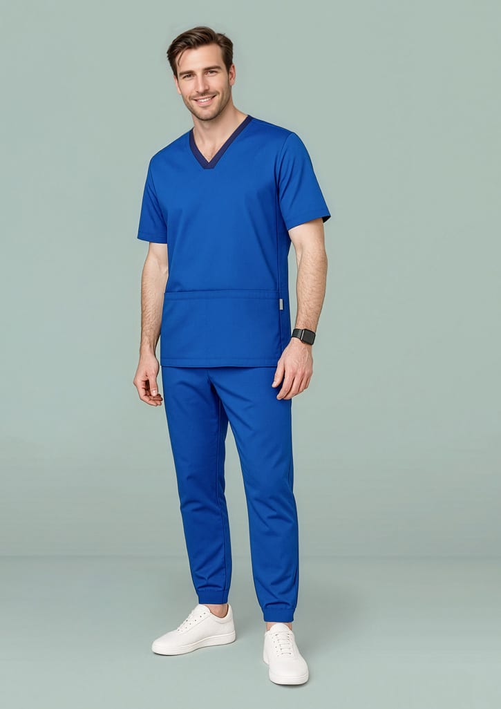 A man in a blue scrub top and slim leg jogger scrub pants, wearing white sneakers, standing against a green background. Mens Riley Slim Leg Jogger Scrub Pant - Image 1