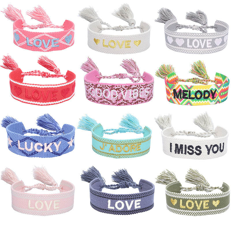 A collection of embroidered bracelets with tassels featuring various colours and messages, including pink, white, and blue. Embroidery Bracelet with Tassels - Image 1