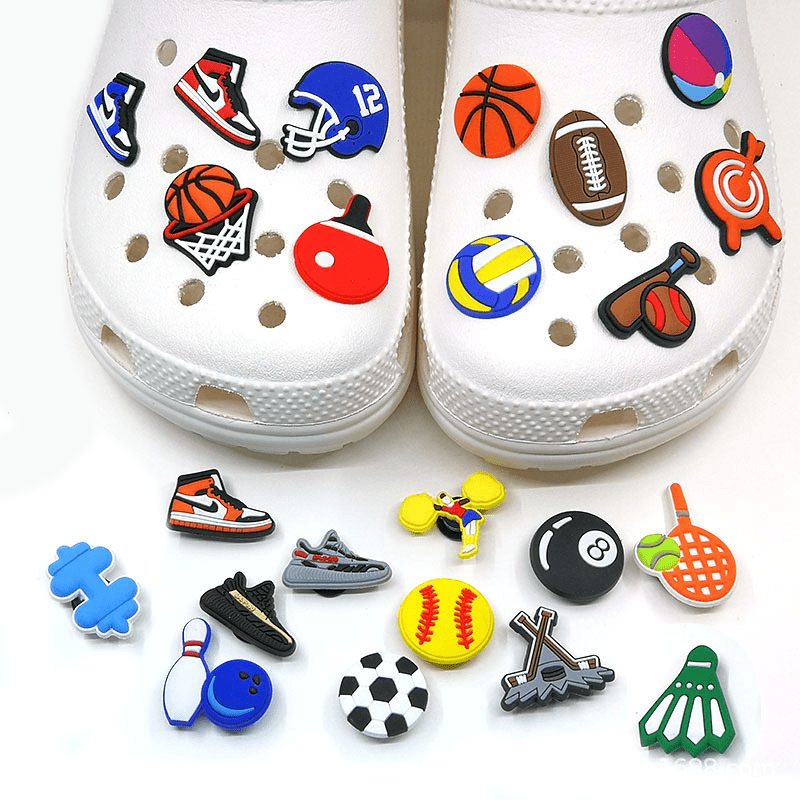 A pair of white Crocs adorned with colourful sports-themed charms, including basketballs, soccer balls, and more. Personality Croc Charms - Image 1