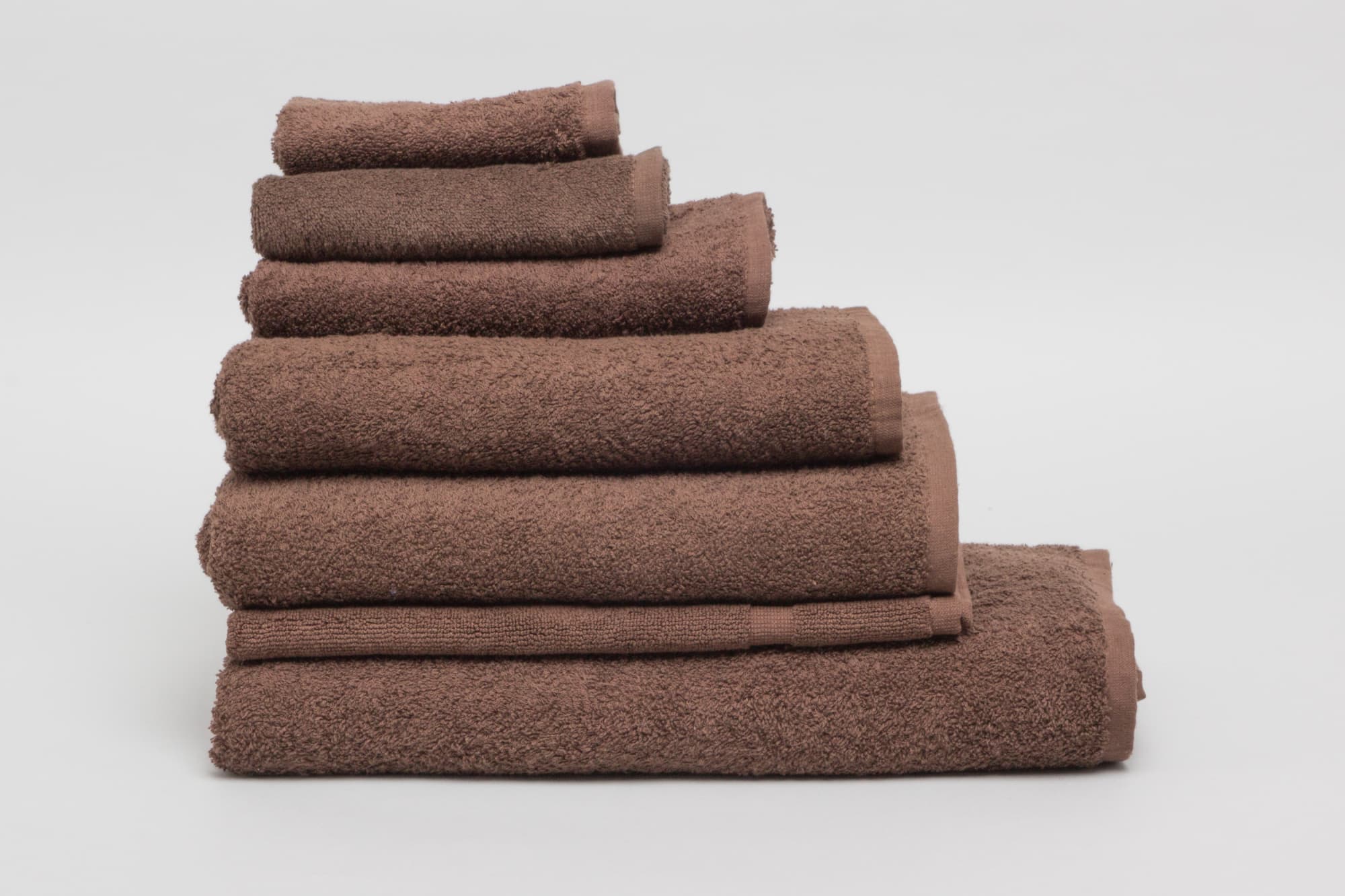 A stack of chocolate brown towels in various sizes with a textured finish, featuring a logo. Elite Bath Mat 500 gsm Chocolate - Image 1