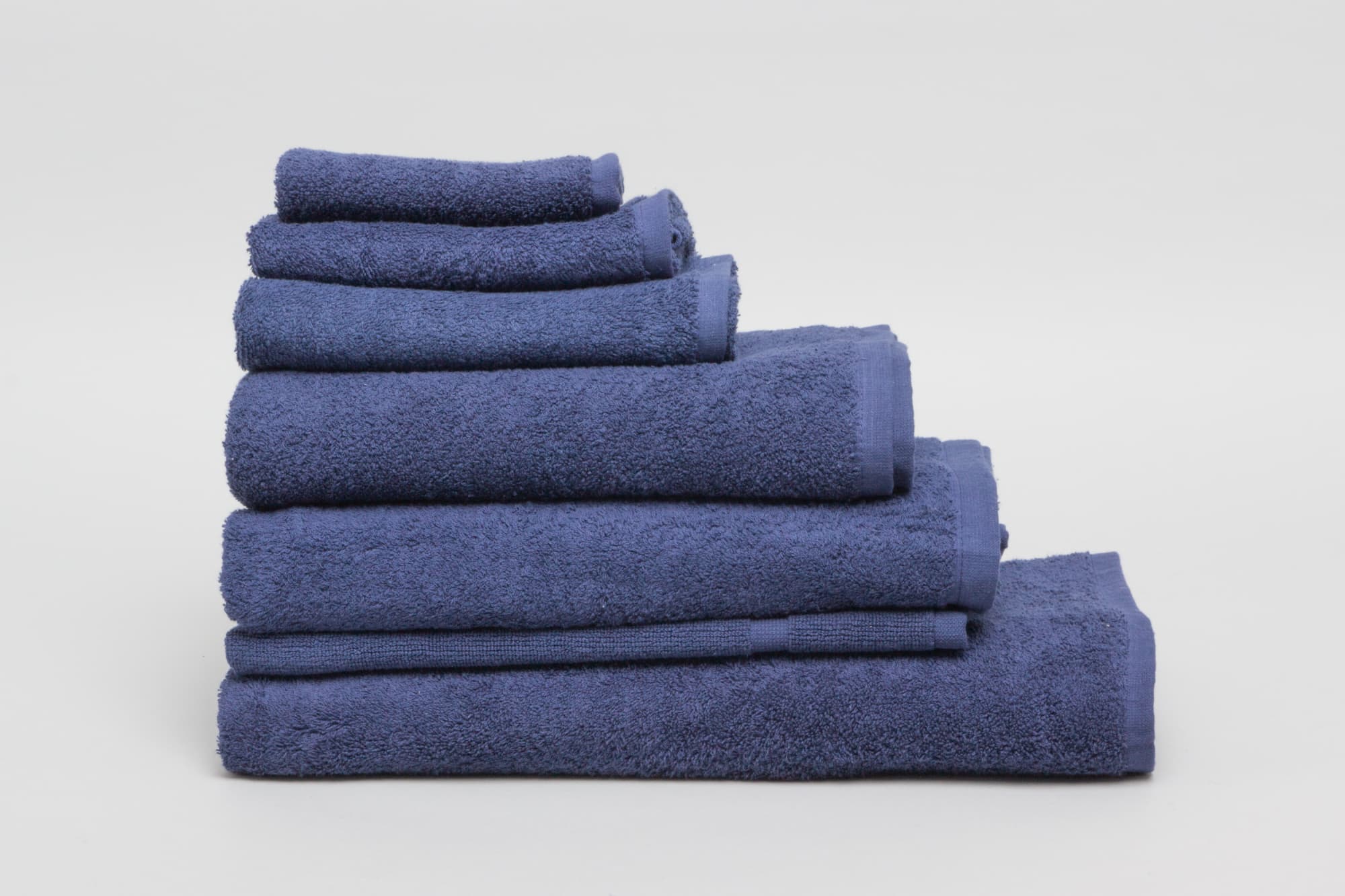 A stack of navy towels in various sizes, featuring a soft texture and a neat presentation. Elite Bath Mat 500 gsm Navy - Image 1