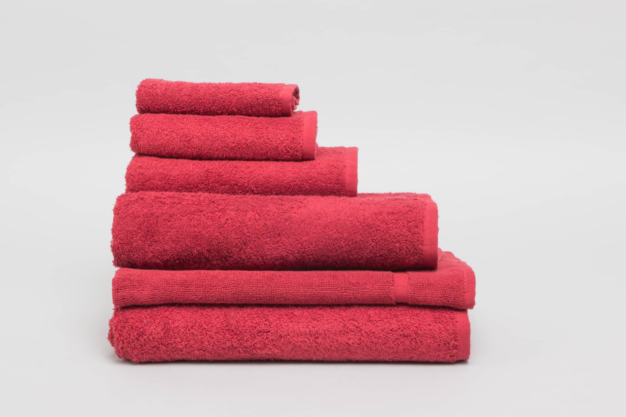 A collection of burgundy bath towels stacked neatly, showcasing various sizes and a soft, textured appearance. Elite Bath Sheet 500 gsm Burgundy - Image 1